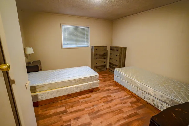 Interior room featuring wood-finish flooring, neutral wall paint, and a window with horizontal blinds
