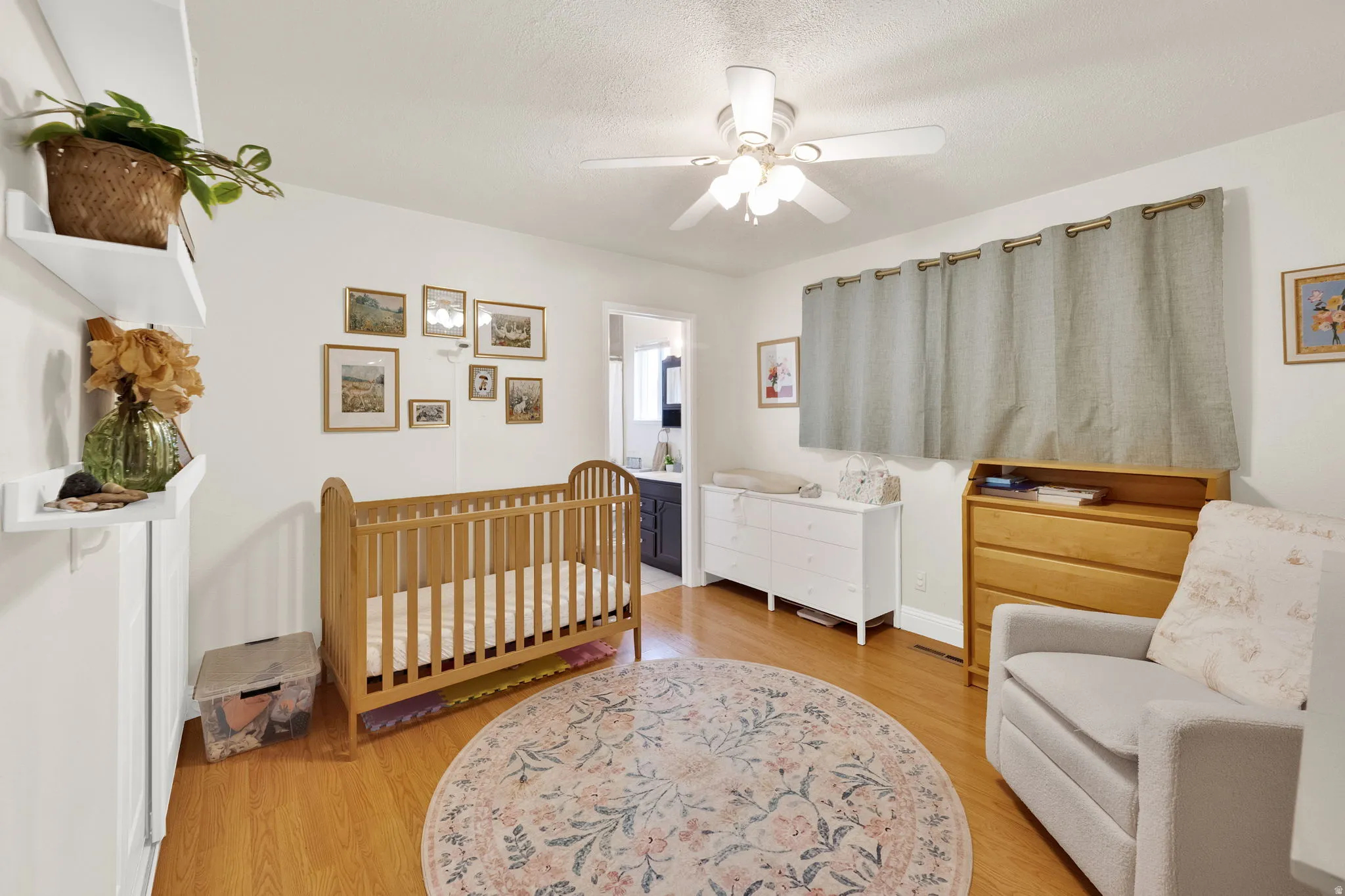 Hardwood-finish flooring featuring a ceiling fan with integrated lighting, wall-mounted floating shelves, and a doorway opening to an adjacent room