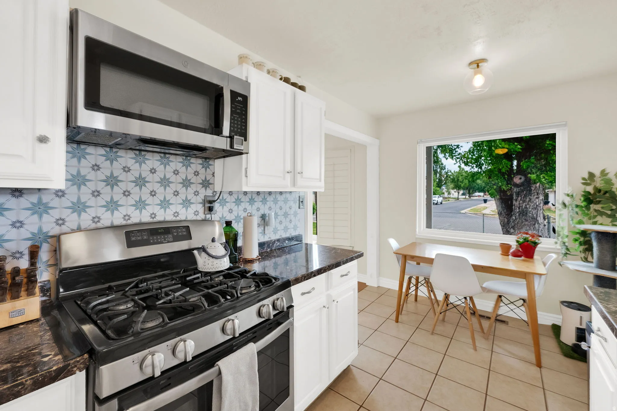 Updated kitchen showcasing white cabinetry, stainless steel appliances, patterned tile backsplash, dark countertops, and tile flooring