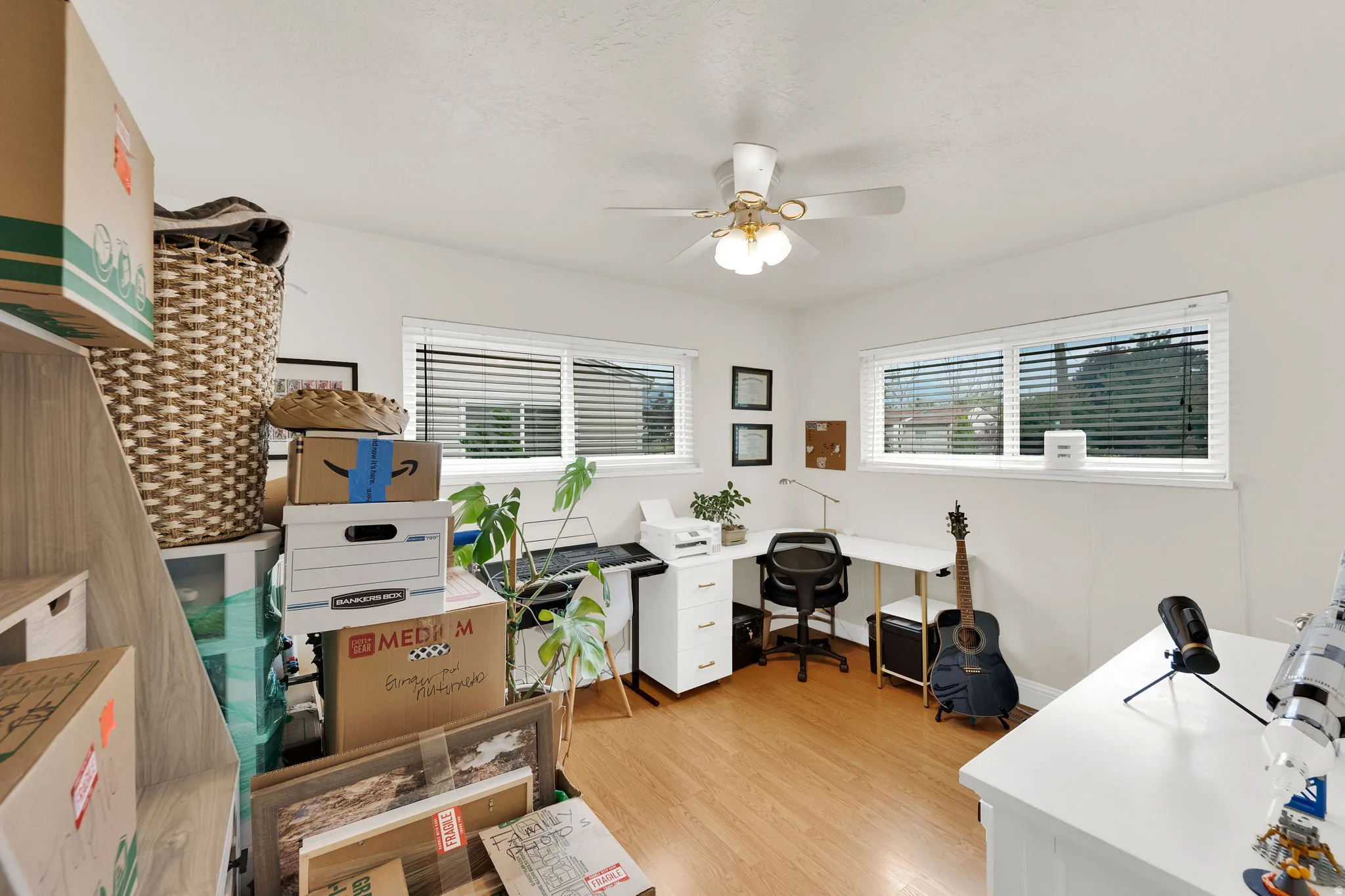 Bright room featuring wood-finish flooring, multiple windows with blinds, and a ceiling fan with integrated lighting