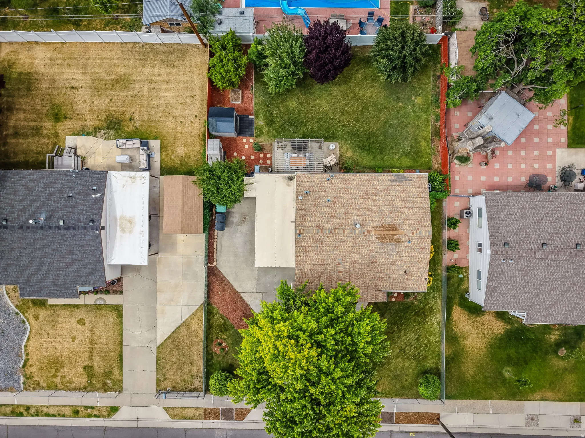 Overhead perspective highlighting the property with a brown shingle roof, a large green tree, and concrete driveways