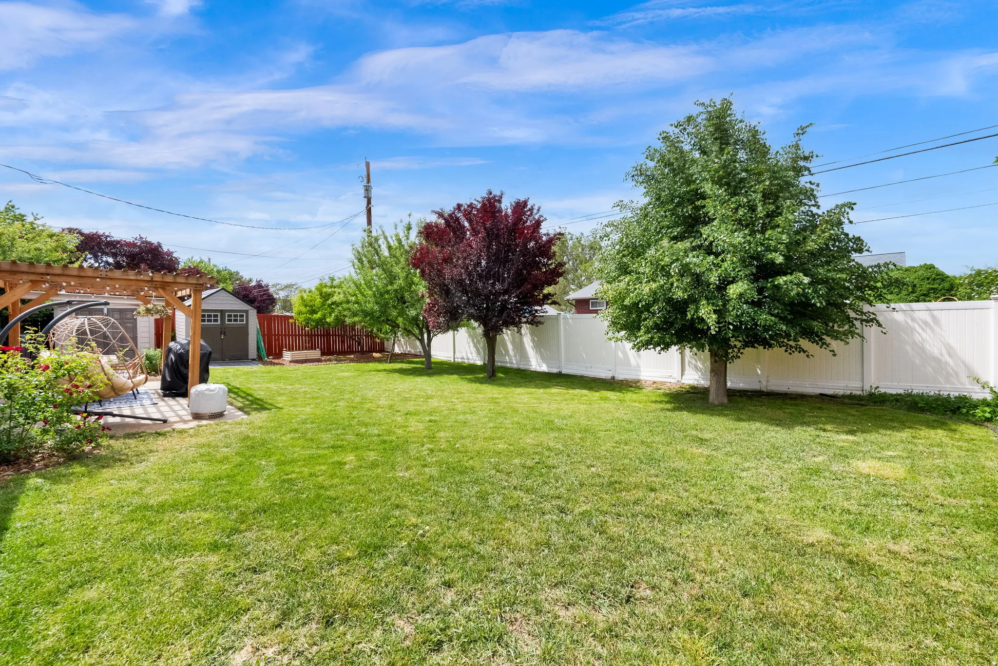 Expansive backyard featuring a manicured lawn, established trees, and a wooden pergola over a paved patio