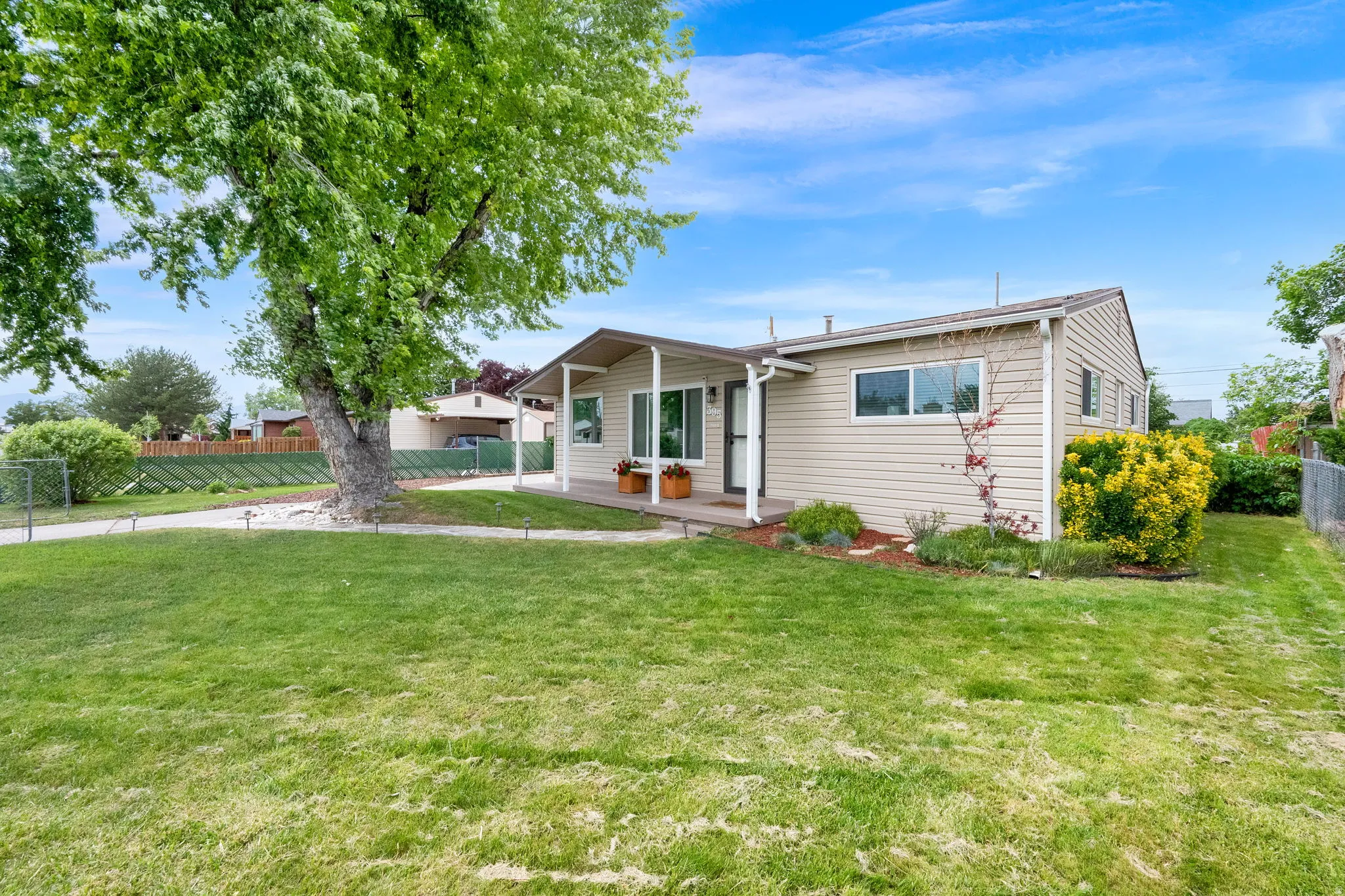 Ranch-style exterior with beige siding, a covered front porch, and a mature shade tree