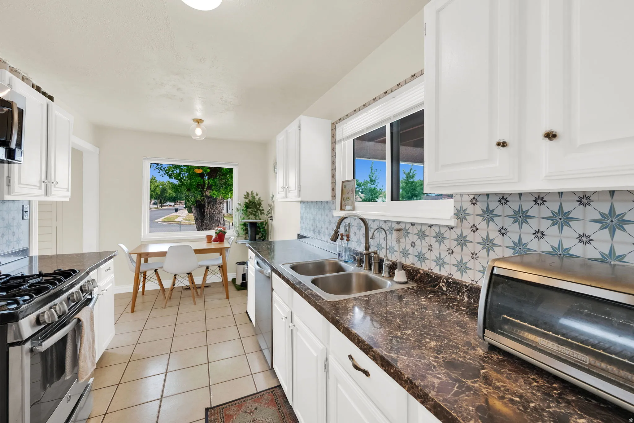 Kitchen featuring white cabinetry, patterned tile backsplash, dark countertops, and stainless steel appliances
