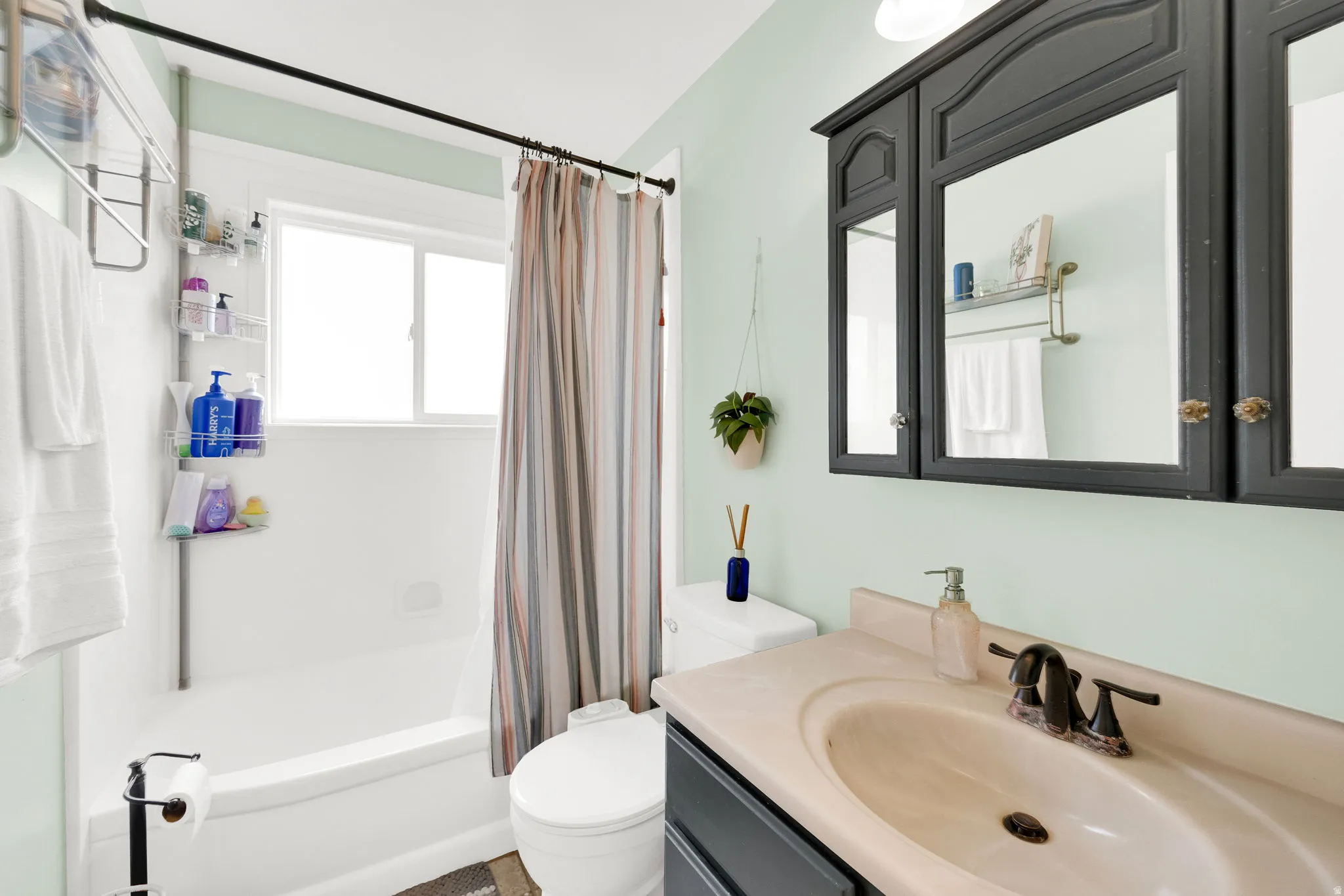 Bathroom featuring a vanity with an integrated sink, a dark medicine cabinet, and a white bathtub with a window