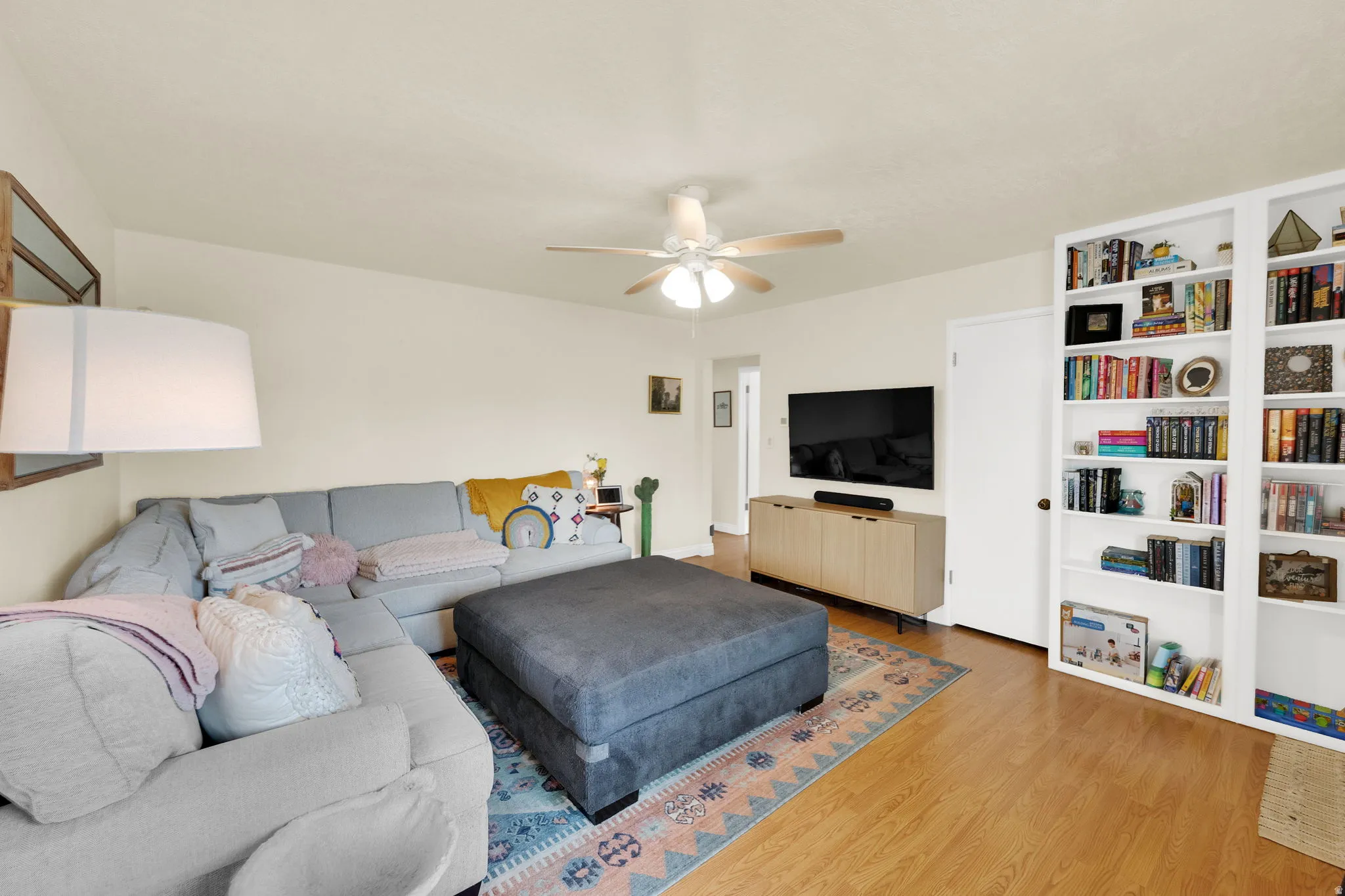 Living area featuring wood-finish flooring, a ceiling fan with light fixture, and built-in white shelving