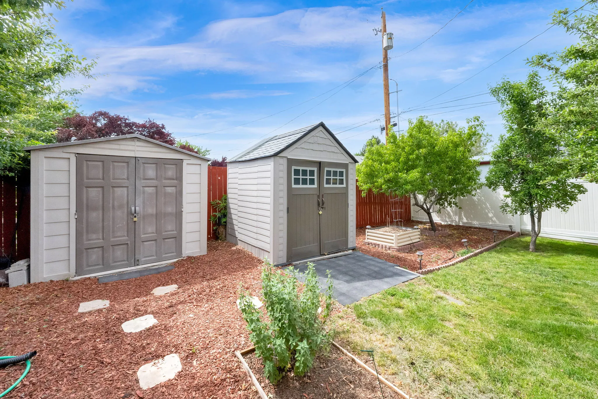 Backyard featuring two storage sheds, a raised garden bed, and a manicured lawn