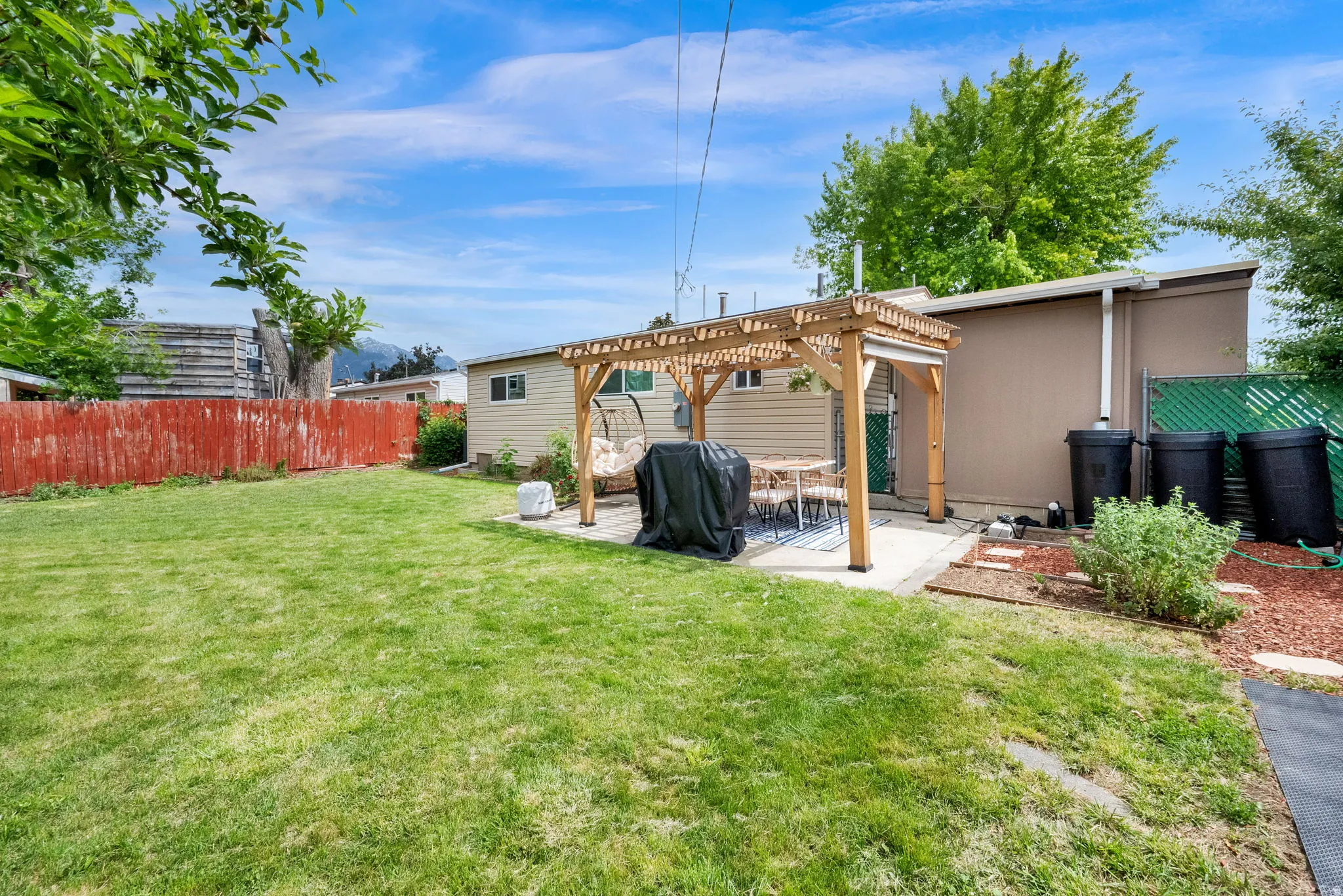 Expansive green lawn with a red perimeter fence, concrete patio, and a wooden pergola structure