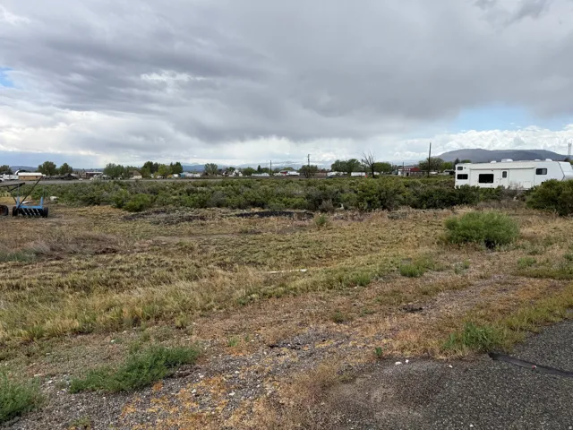 Expansive undeveloped land with natural vegetation, featuring distant structures and mountainous terrain under a cloudy sky
