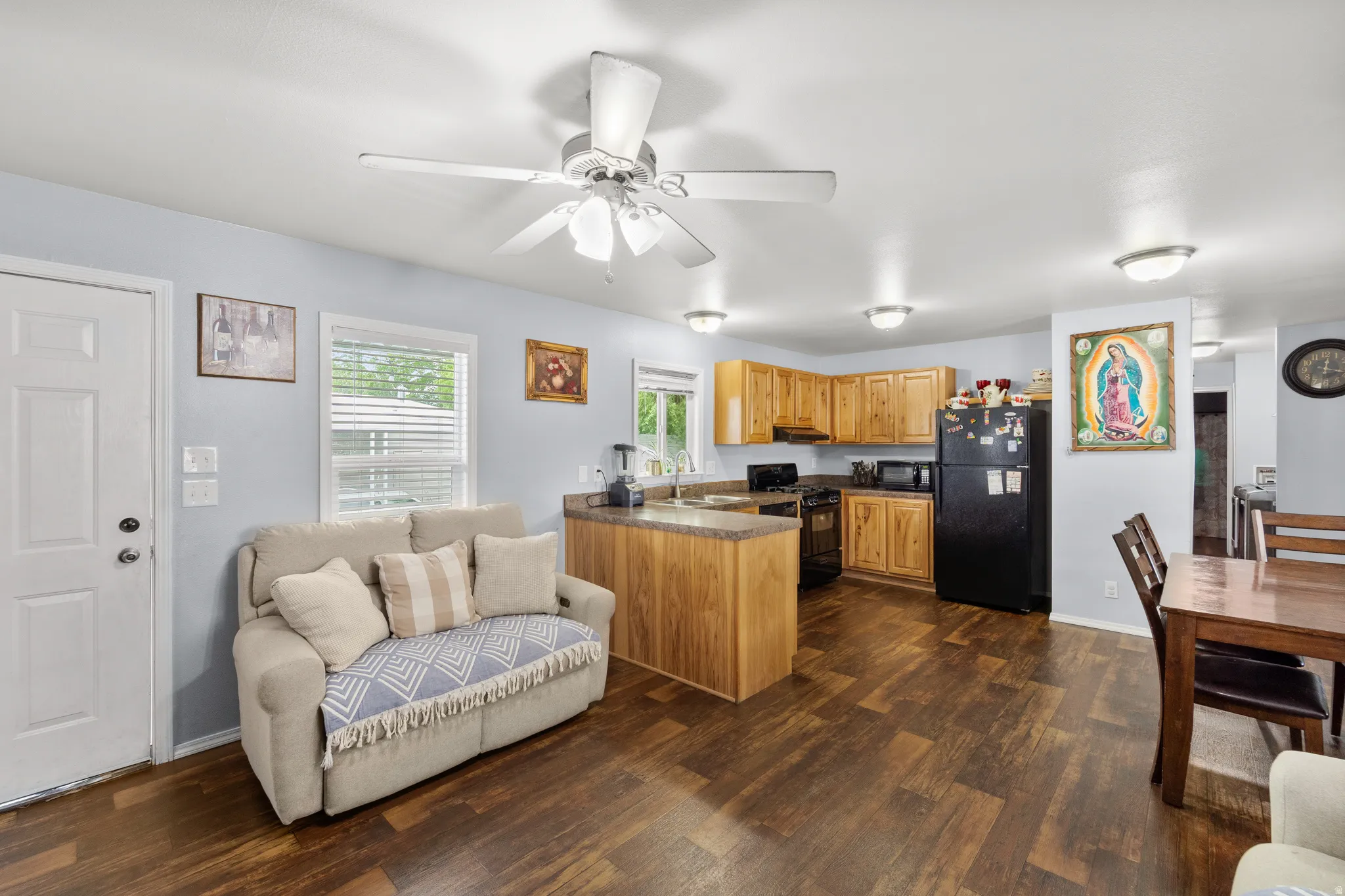 Open-concept kitchen and living area featuring wood-finish flooring, light-toned cabinetry, and a ceiling fan with integrated lighting