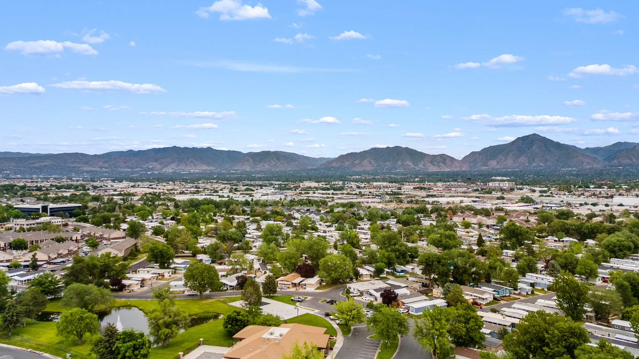 Expansive aerial perspective showcasing a residential area with varied housing structures, mature trees, and a prominent mountain range backdrop