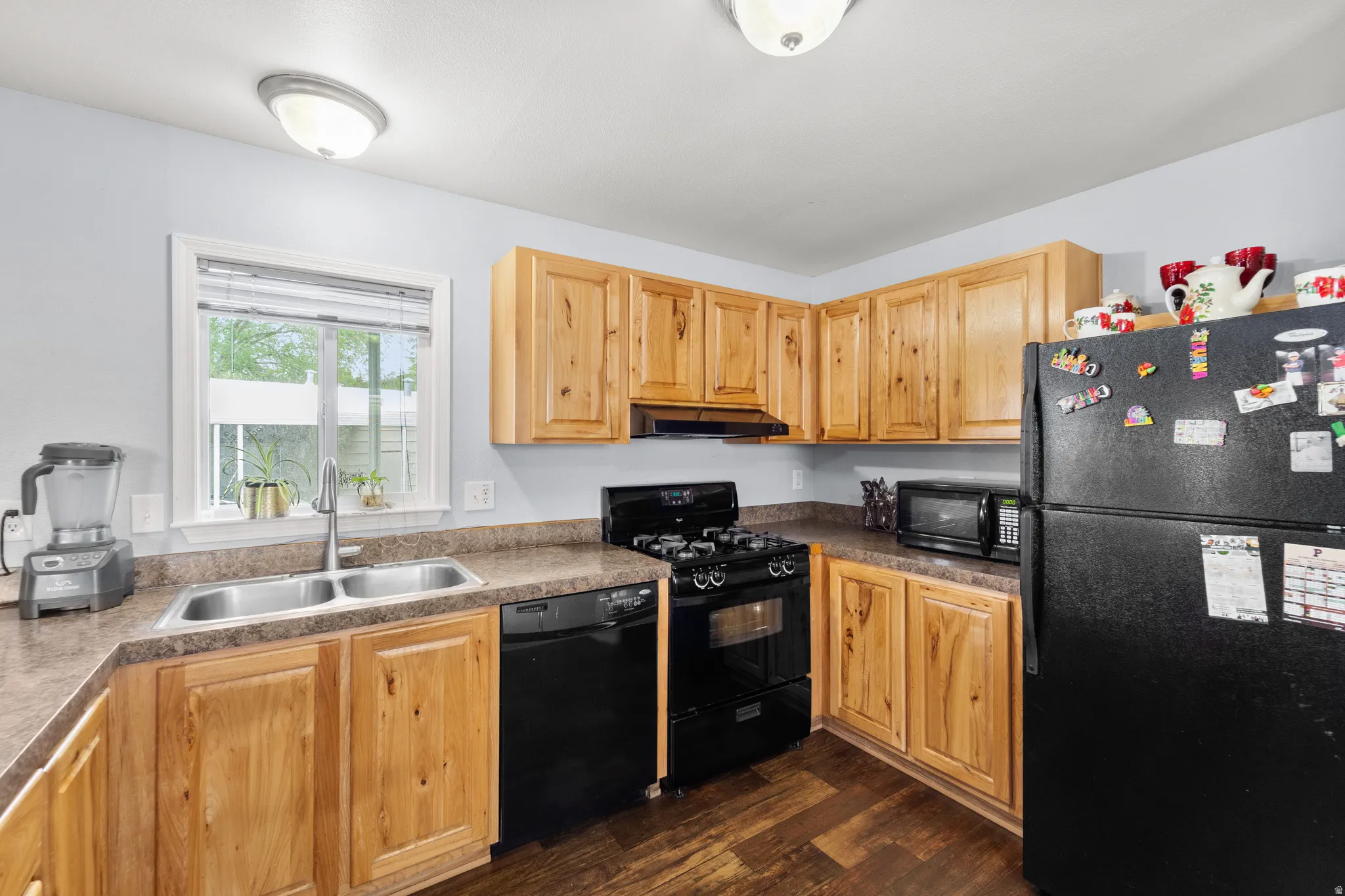 Kitchen featuring wood-finish cabinetry, black appliances, a double-basin stainless steel sink, and wood-finish flooring