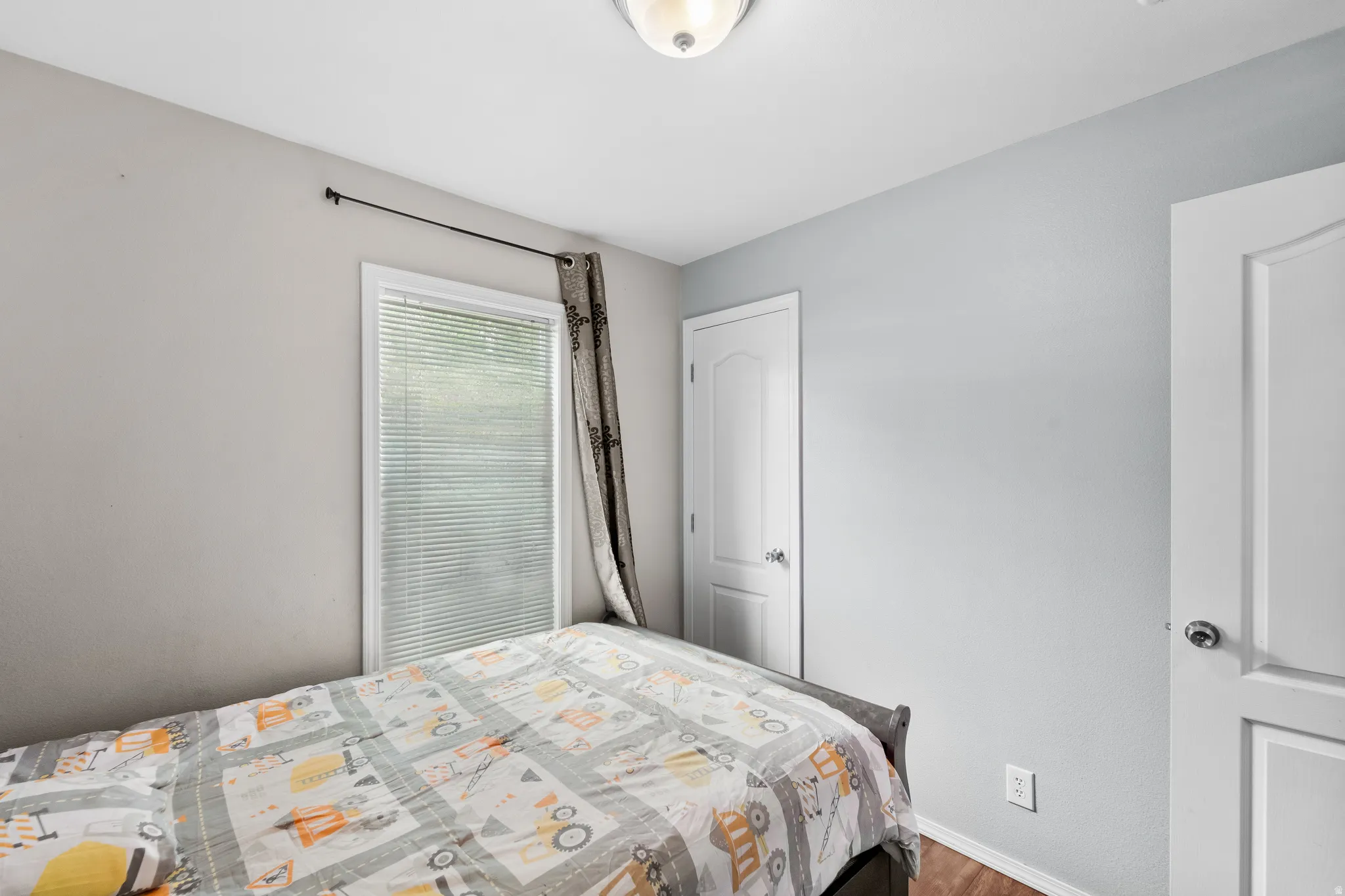 Room featuring a ceiling-mounted light fixture, white window blinds, and wood-finish flooring