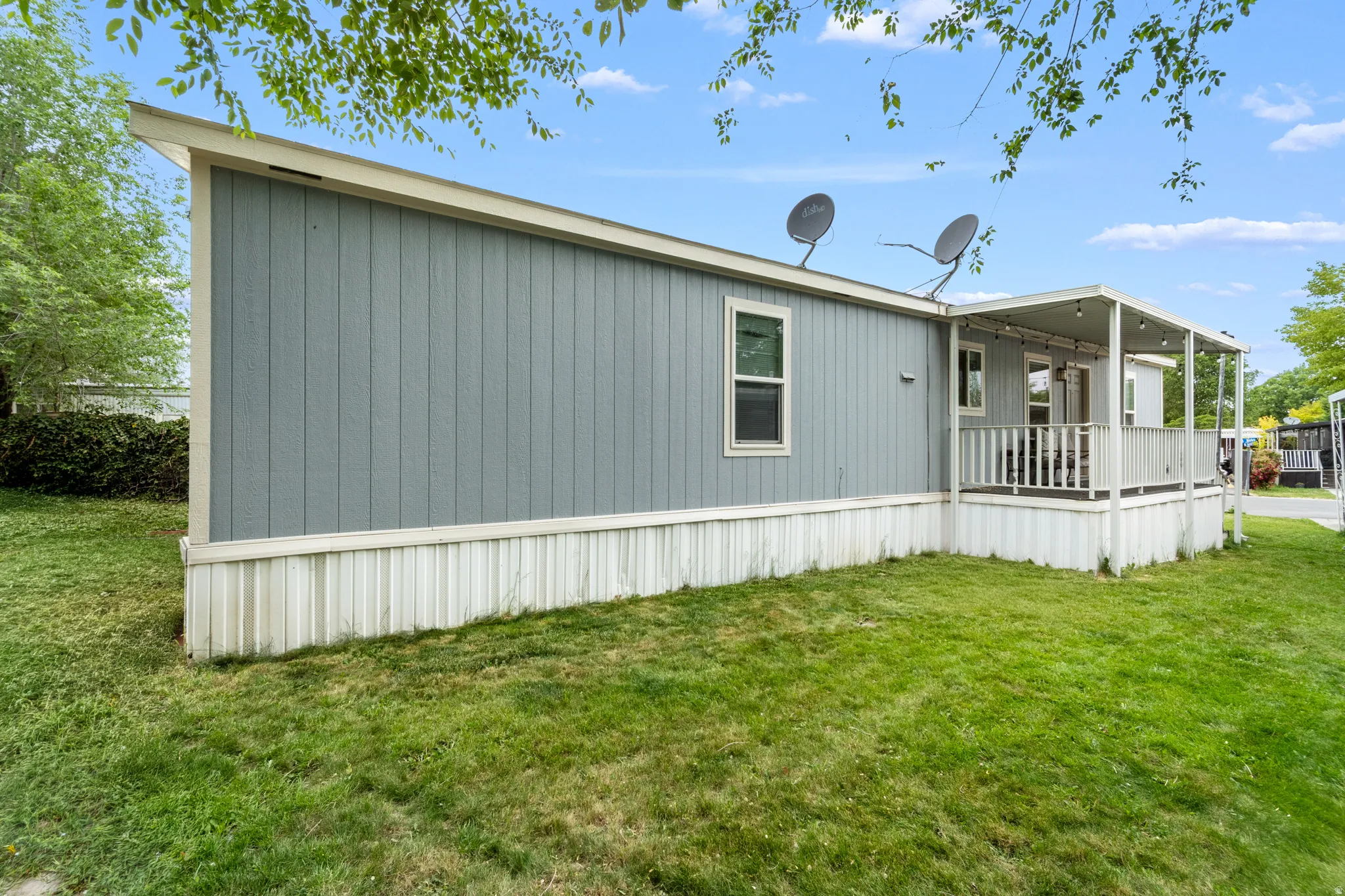 Exterior featuring a covered porch with white railings, blue vertical siding, and a white foundation skirting