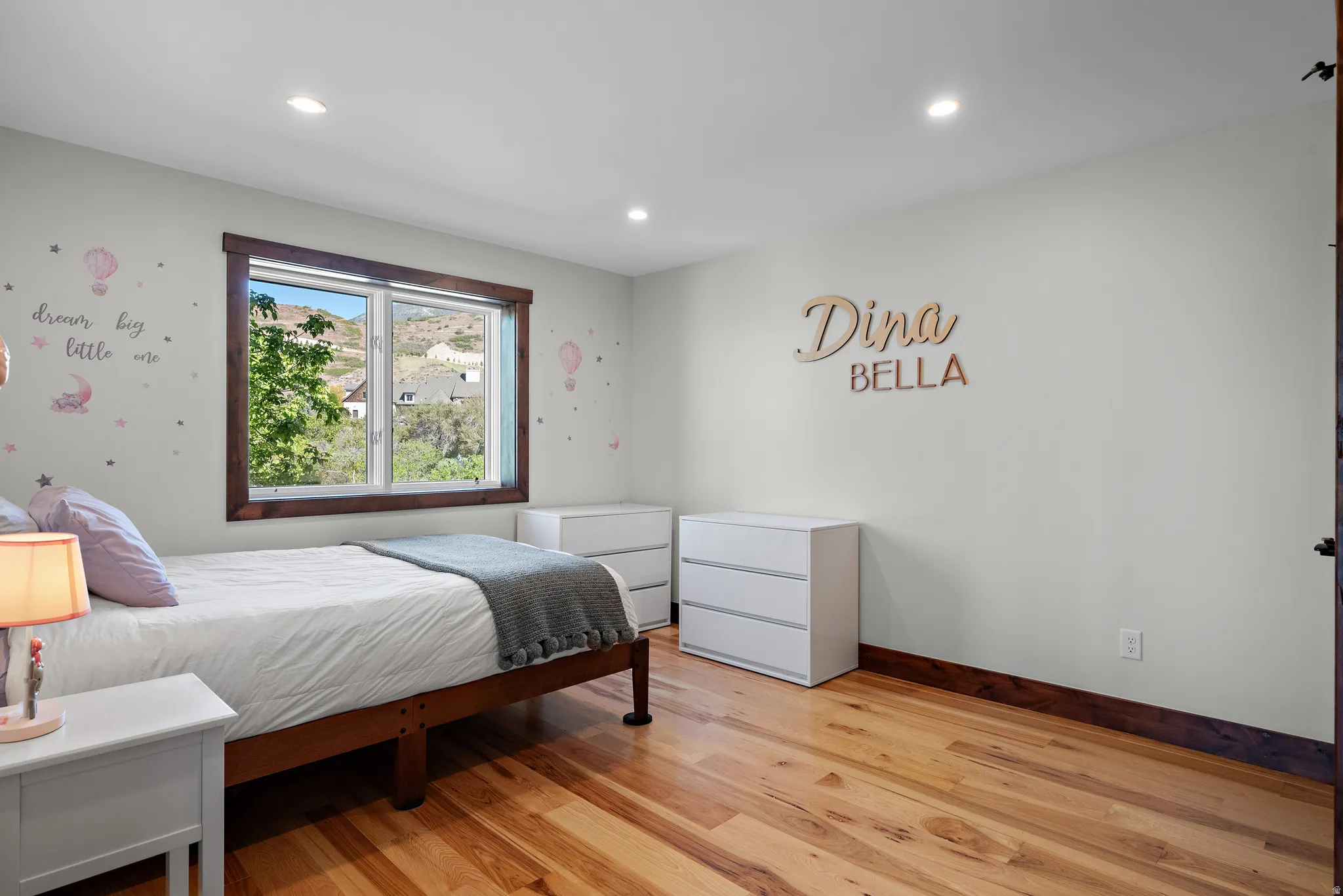 Bright interior space featuring light-toned walls, recessed lighting, wood-finish flooring, and a large window with dark wood trim overlooking distant hillsides