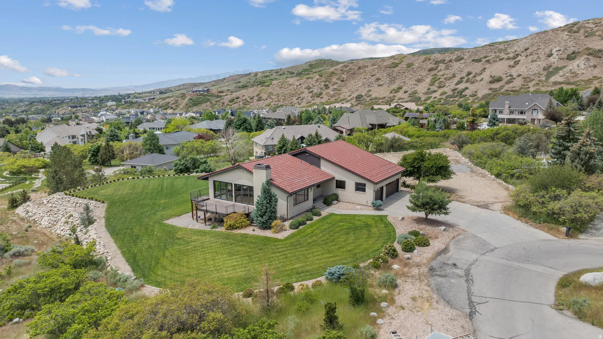 Hillside residence featuring a red tile roof, stucco exterior, and an expansive sloped lawn