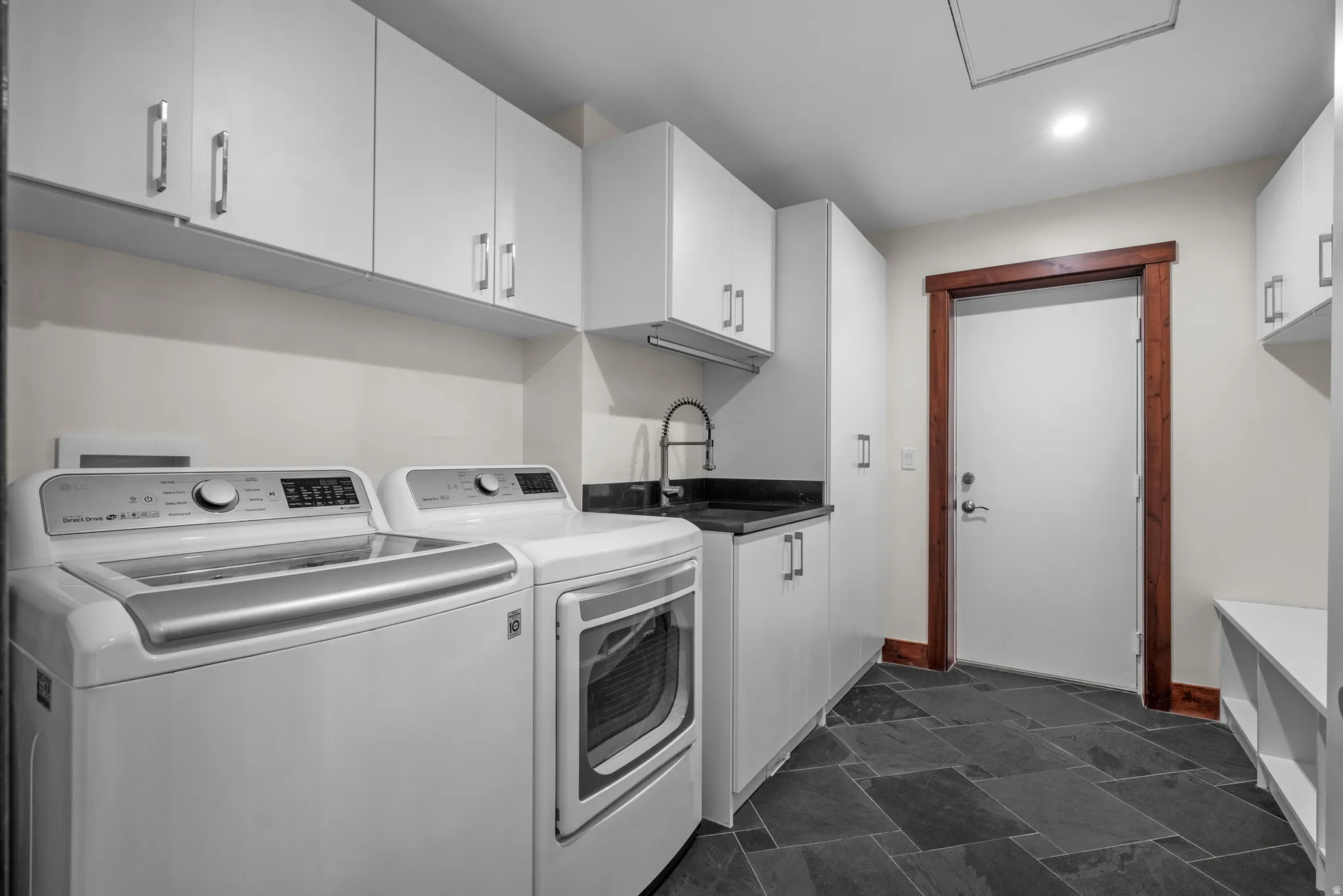 Laundry room featuring dark slate tile flooring, white cabinetry, a utility sink with a black countertop, and a wood-trimmed doorway