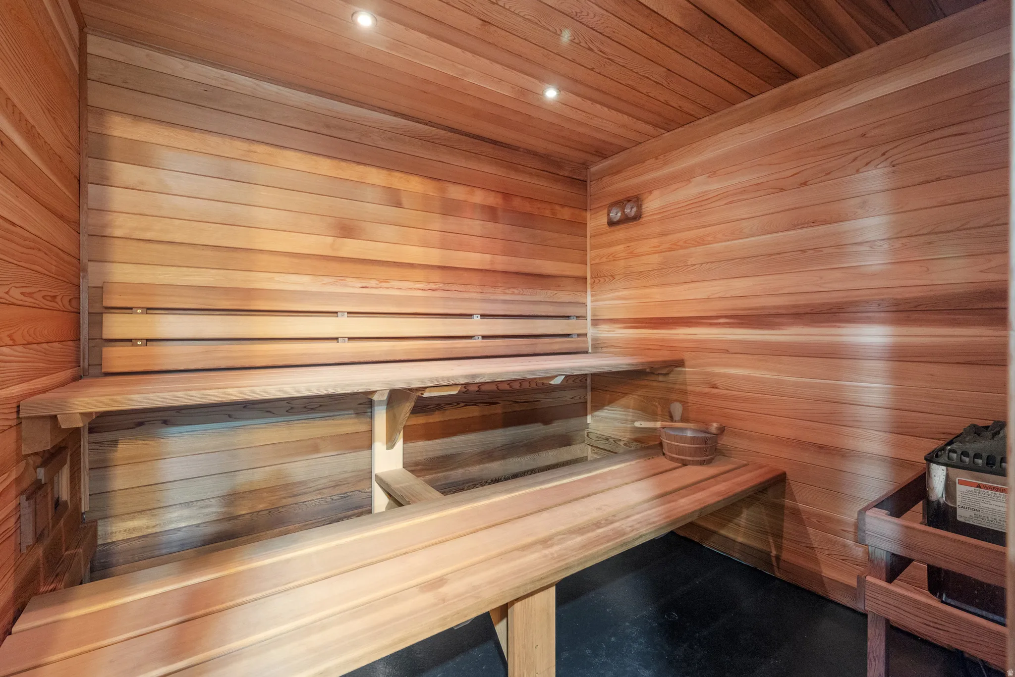 Custom sauna with cedar plank walls and ceiling, multi-level wood benches, and recessed lighting
