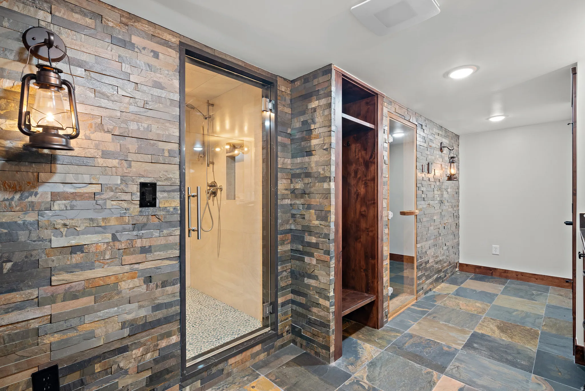 Stone-clad wall featuring a glass-enclosed shower with pebble flooring