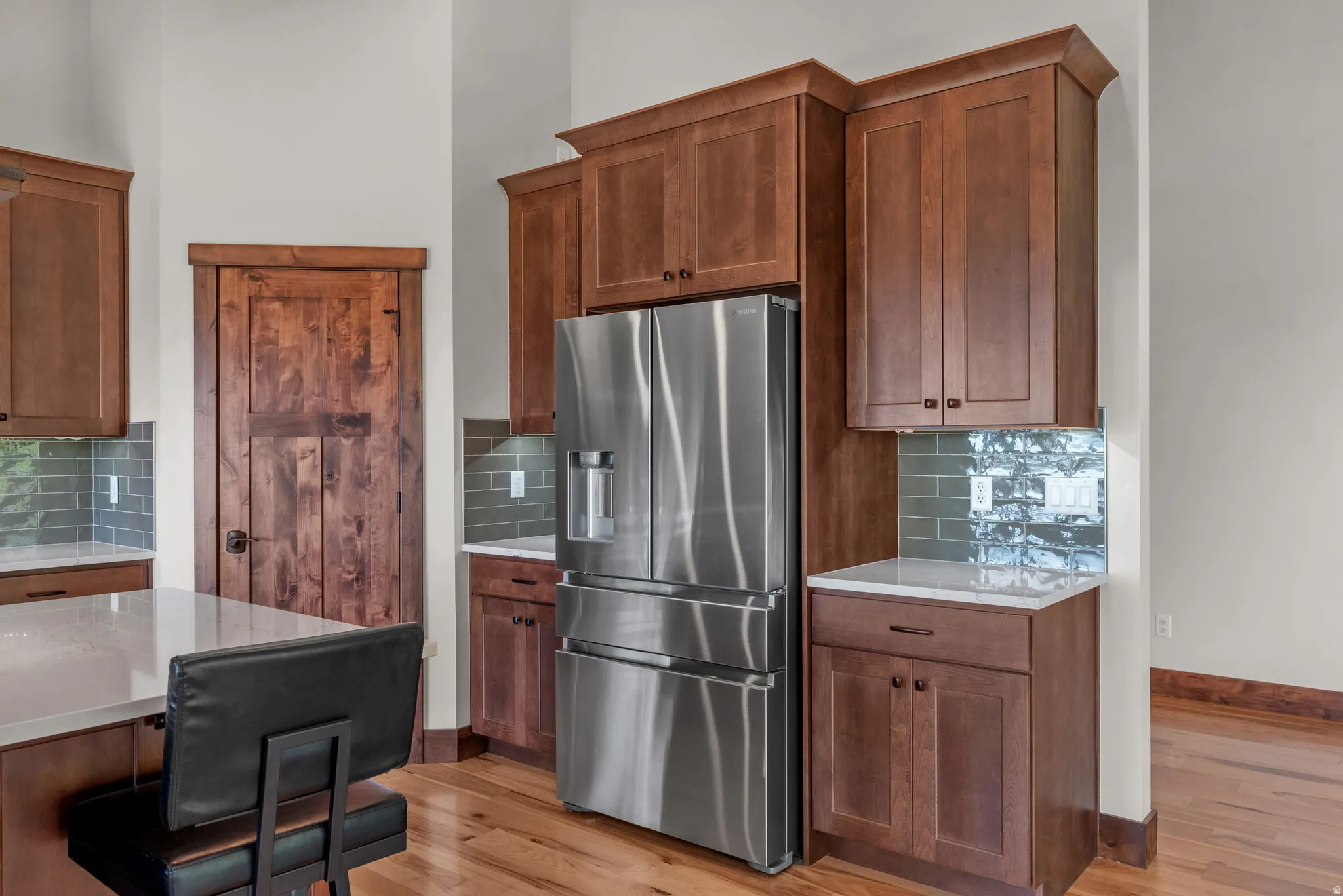 Gourmet kitchen featuring a stainless steel French door refrigerator, extensive wood cabinetry, light-toned countertops, and a tiled backsplash