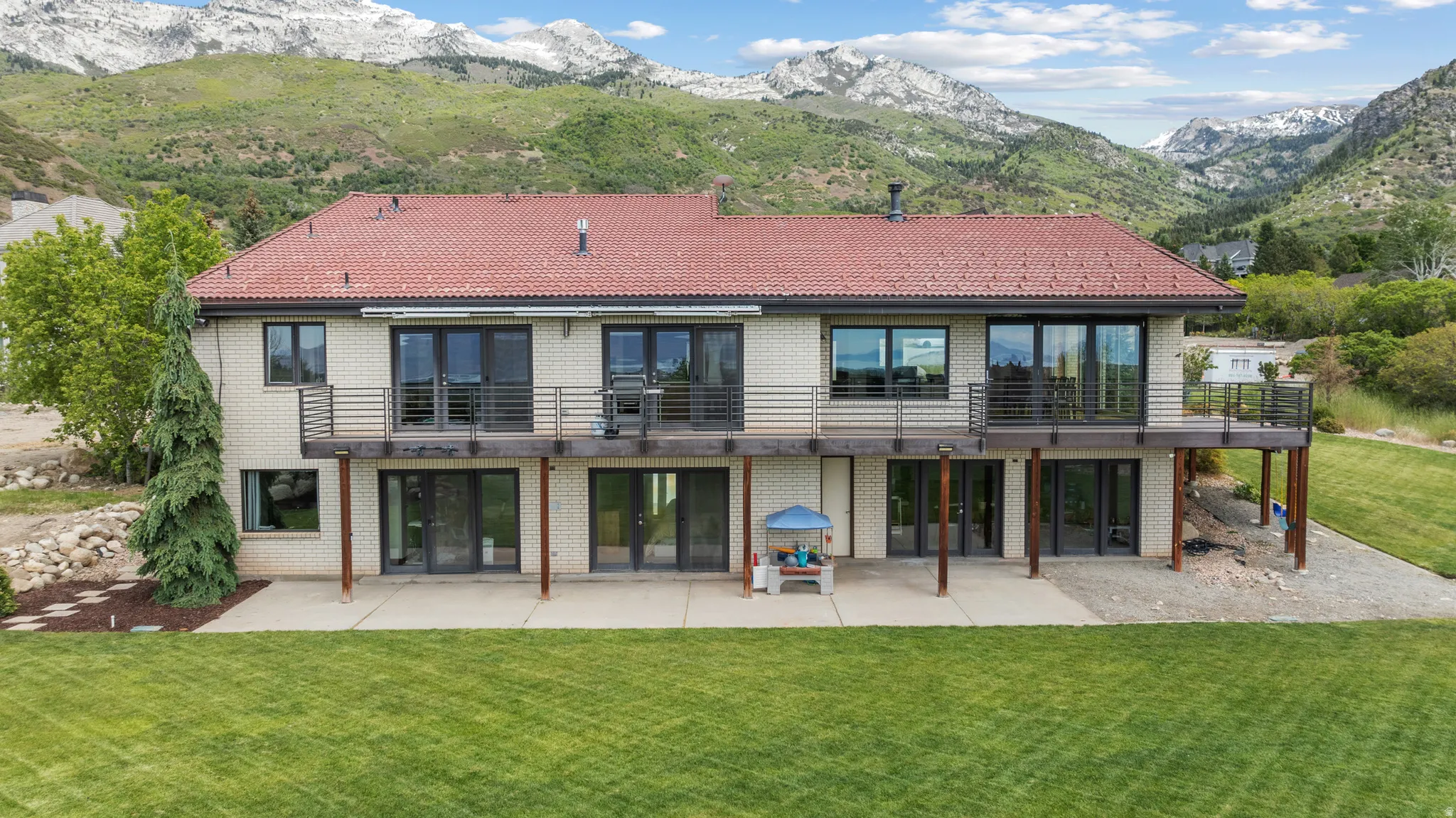 Rear exterior featuring a full-width upper deck with metal railings, ground-level patio space, and a red tile roof
