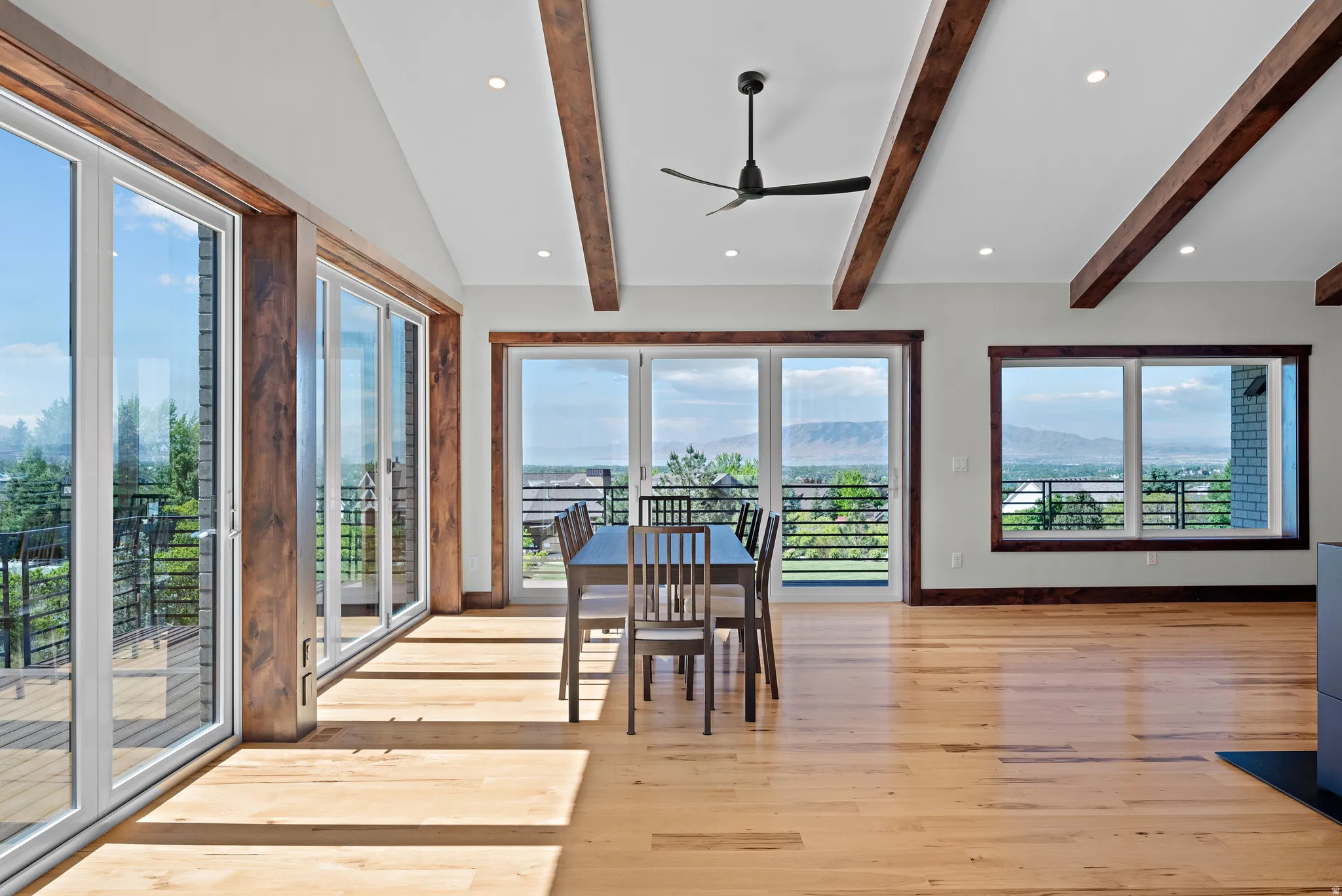 Expansive interior featuring wood-finish flooring, exposed ceiling beams, recessed lighting, and multiple oversized windows and glass doors with mountain scenery
