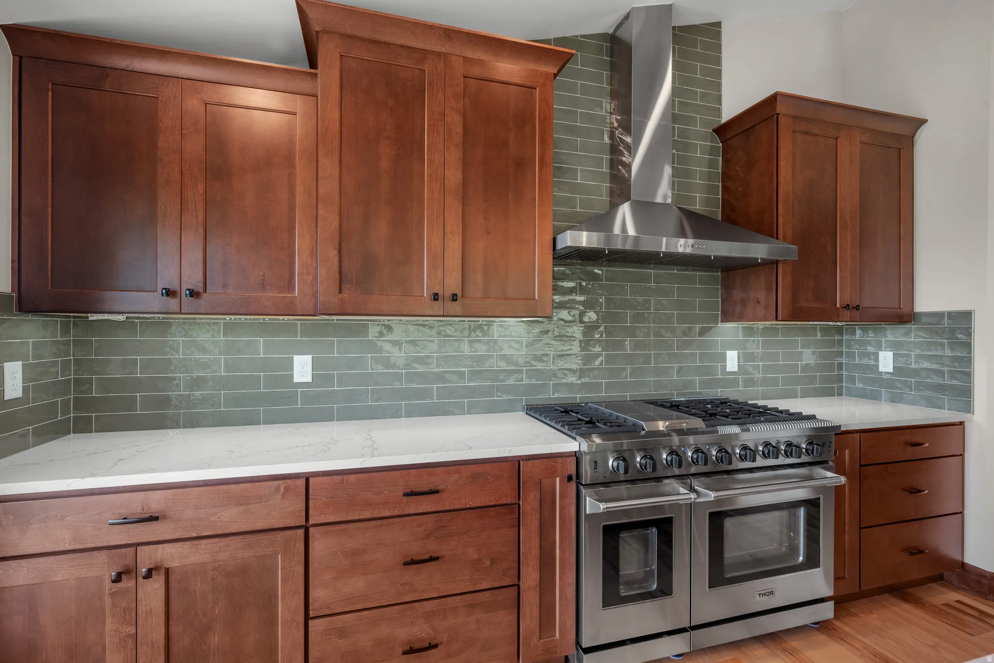 Gourmet kitchen featuring a stainless steel professional-grade range with a matching range hood, ample cabinetry with dark hardware, a subway tile backsplash, and light-toned countertops