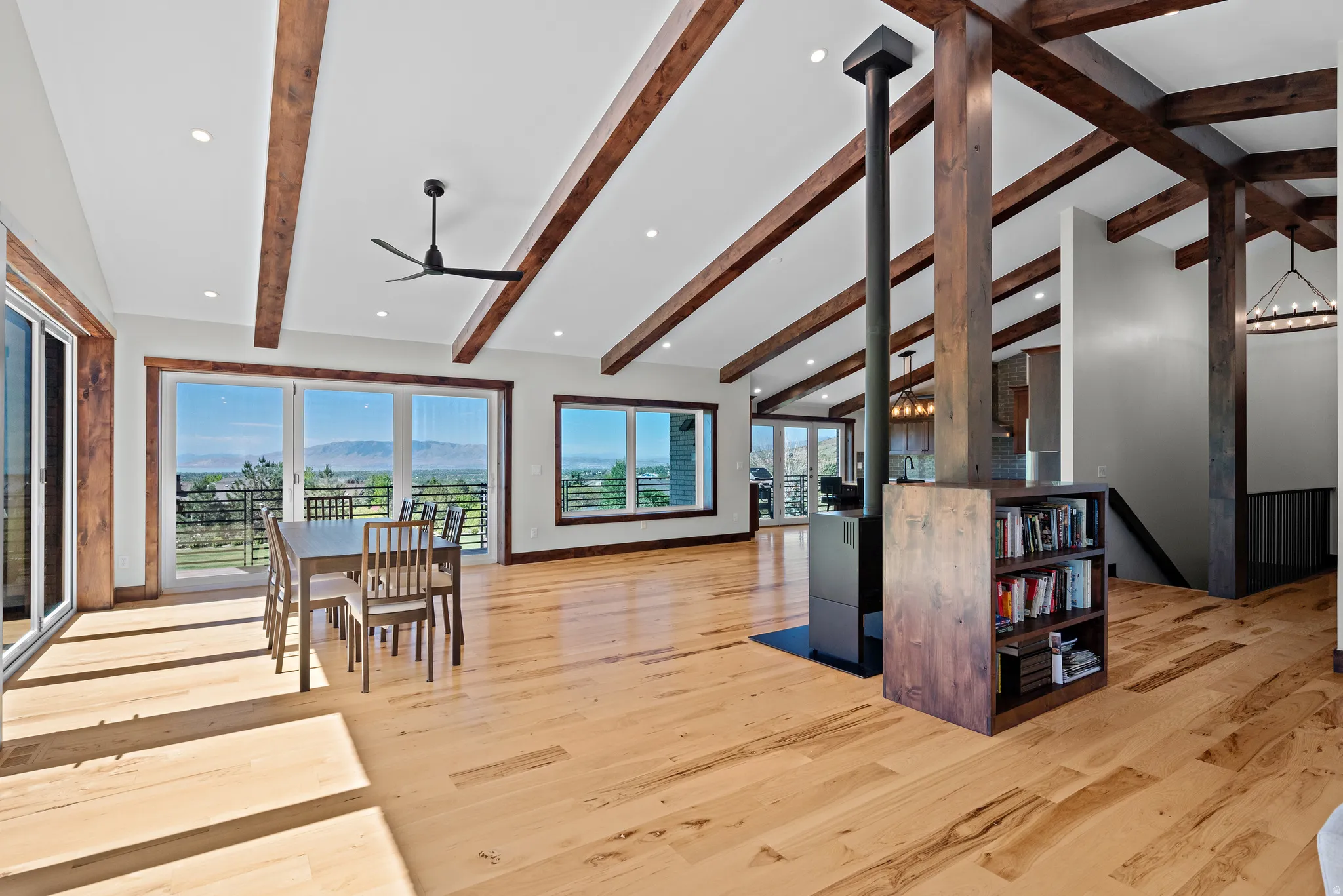 Spacious interior featuring vaulted ceilings with exposed wood beams, light wood-finish flooring, and multiple sliding glass doors