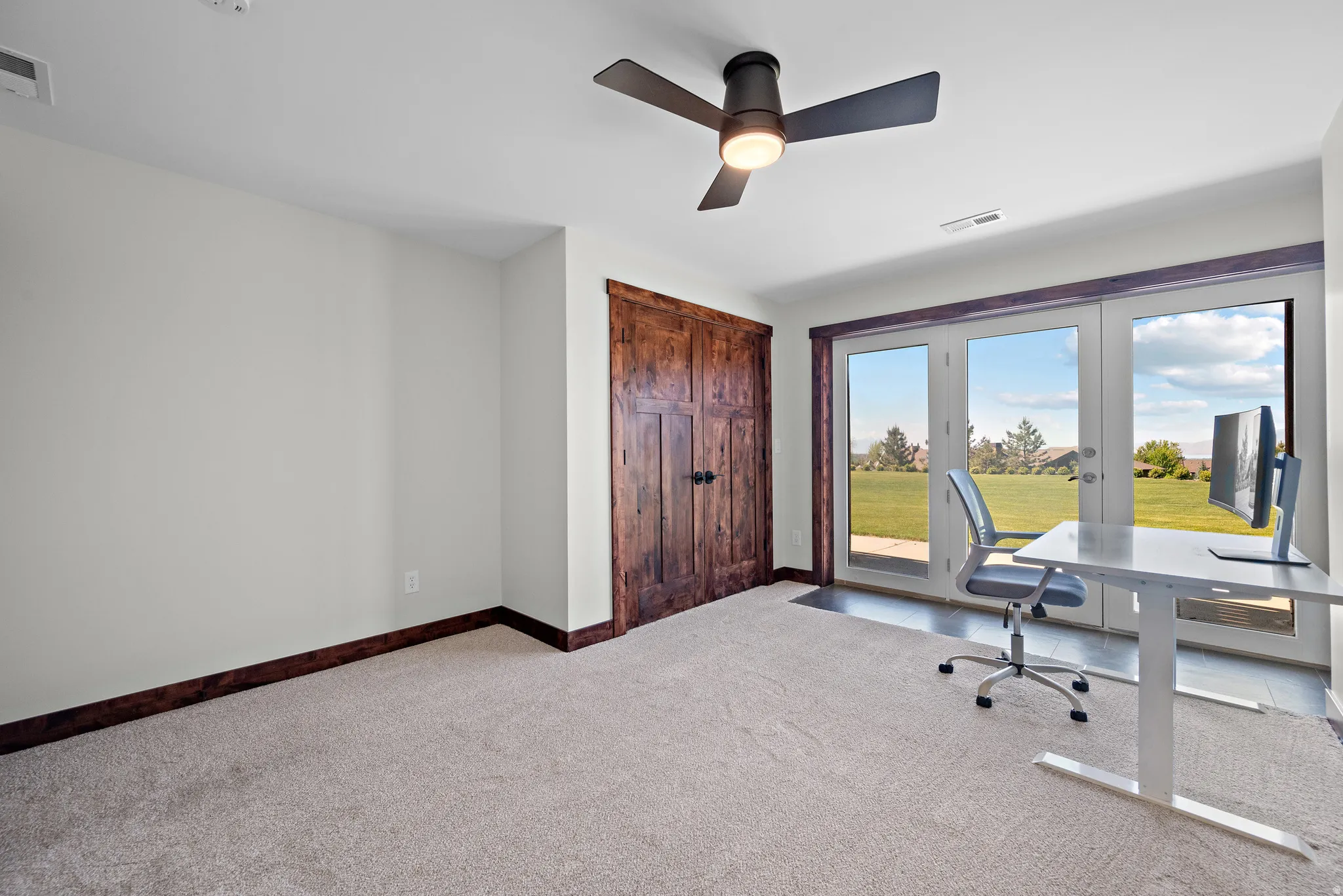 French doors opening to a green landscape, complemented by a ceiling fan with integrated lighting and a wood-paneled door