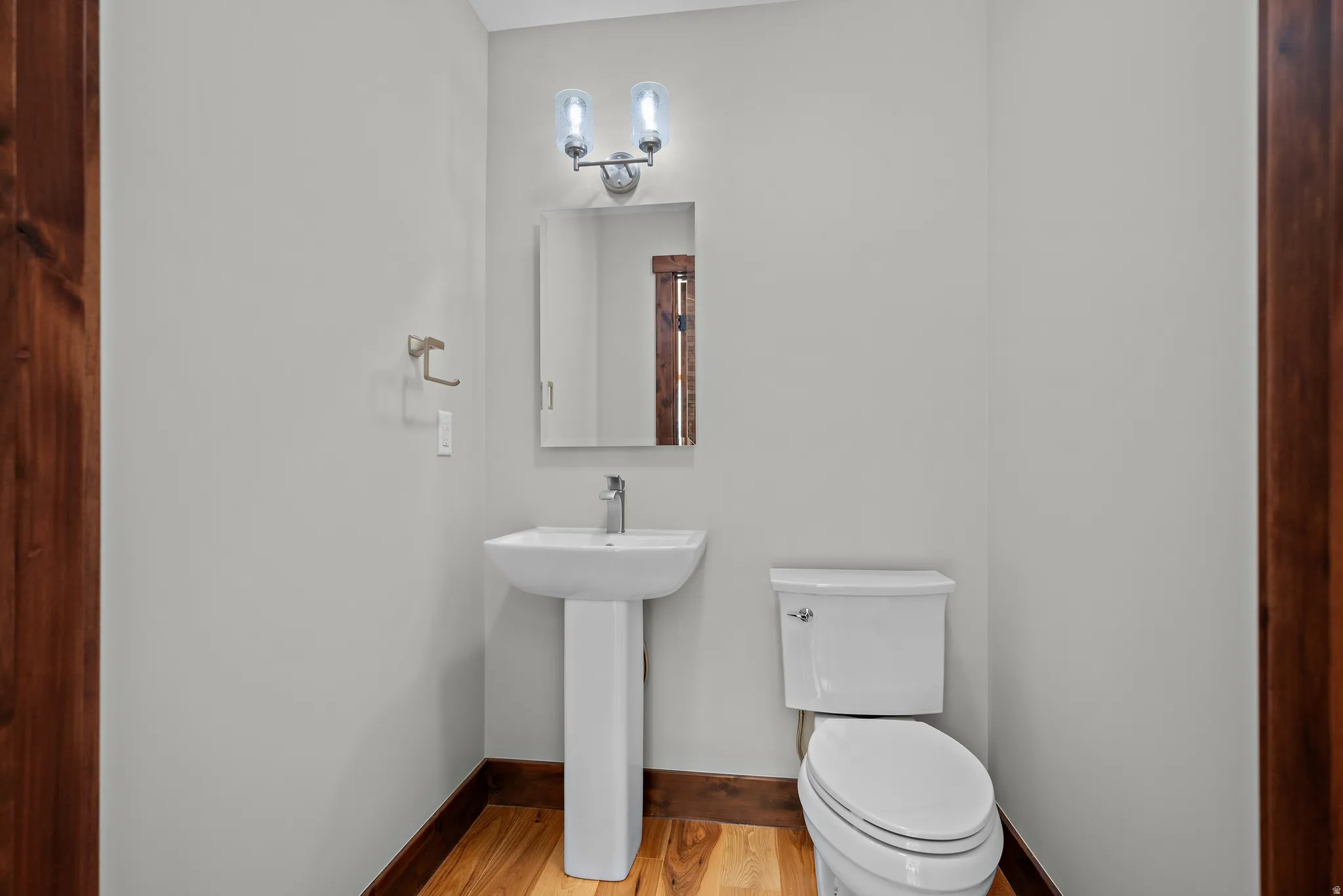 Pedestal sink with a single-handle faucet, rectangular mirror, and an overhead vanity light fixture