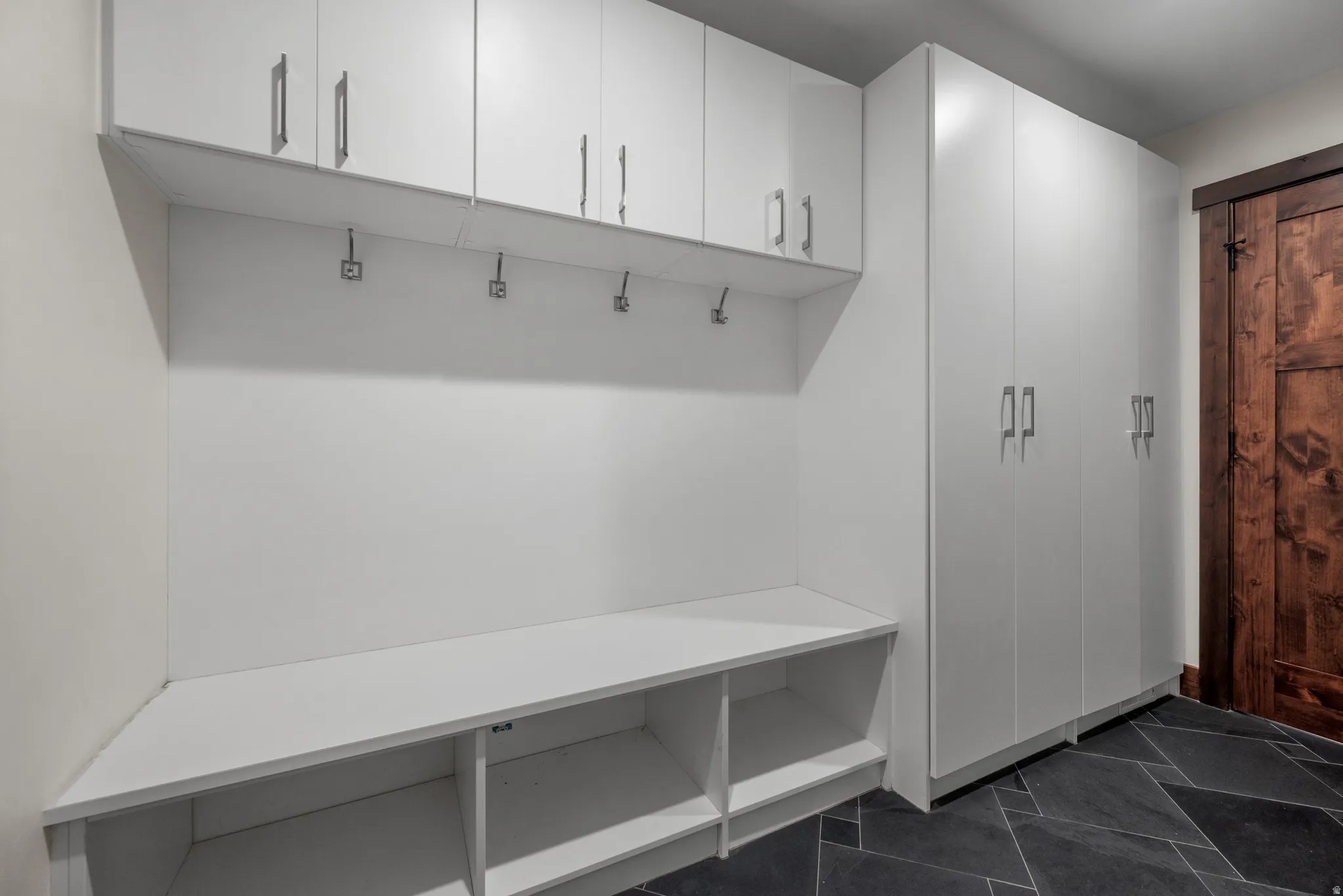 Built-in storage system featuring white cabinetry with silver-tone hardware, an integrated bench with open cubbies, and multiple wall hooks