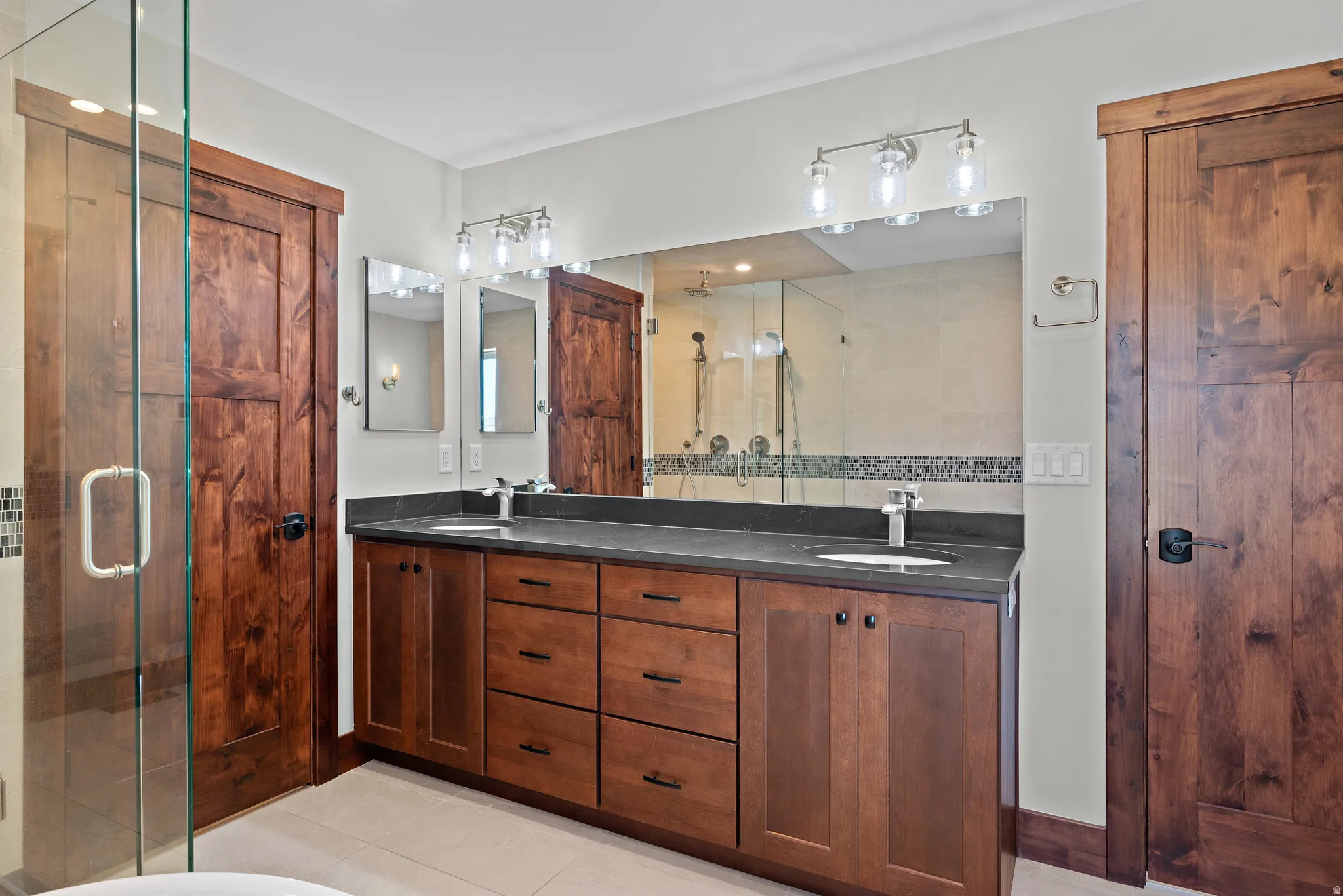 Bathroom featuring a dual vanity with a dark countertop, undermount sinks, and contemporary faucets