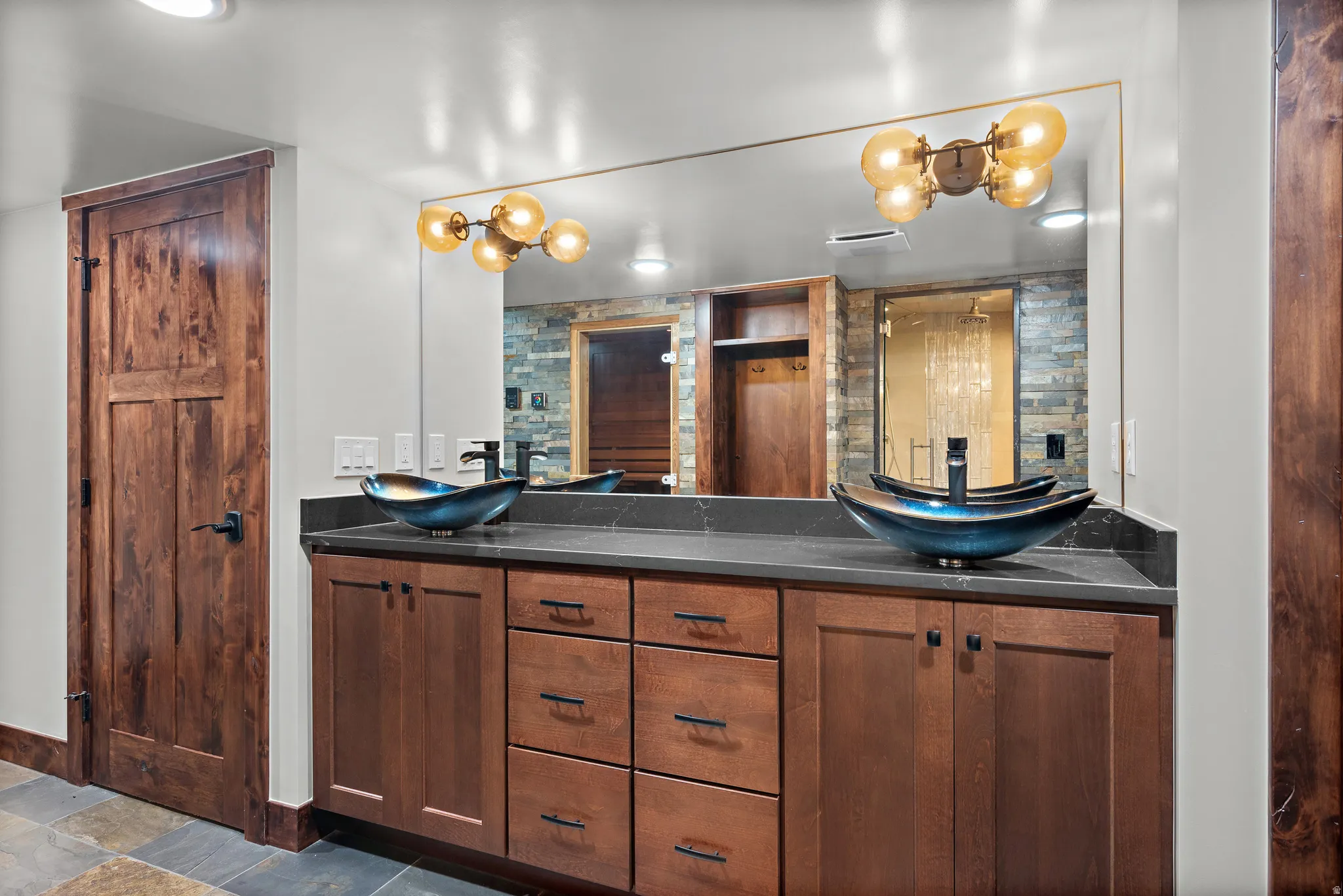 Dual vessel sinks with wall-mounted matte black faucets on a dark countertop