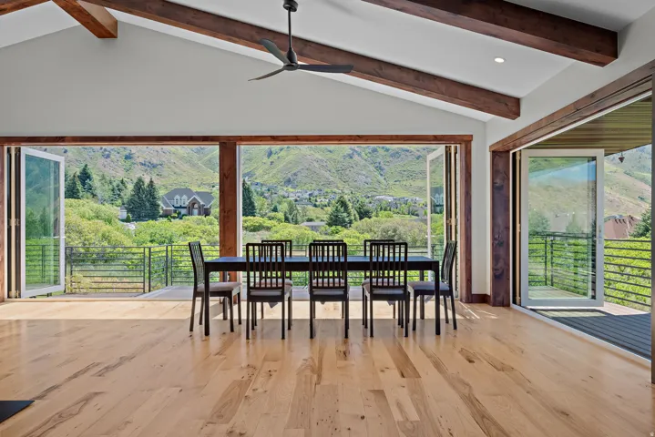 Vaulted ceilings with exposed beams, wood-finish flooring, and folding glass doors opening to a deck with mountain scenery