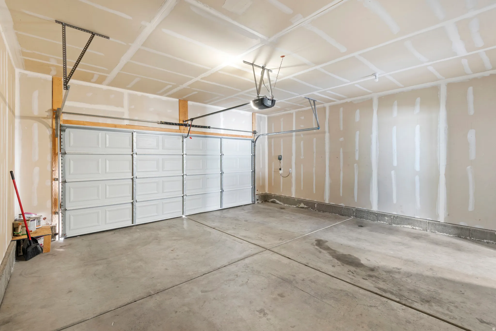 Spacious garage featuring a concrete floor, two white panel garage doors, and an exposed ceiling with an automatic opener