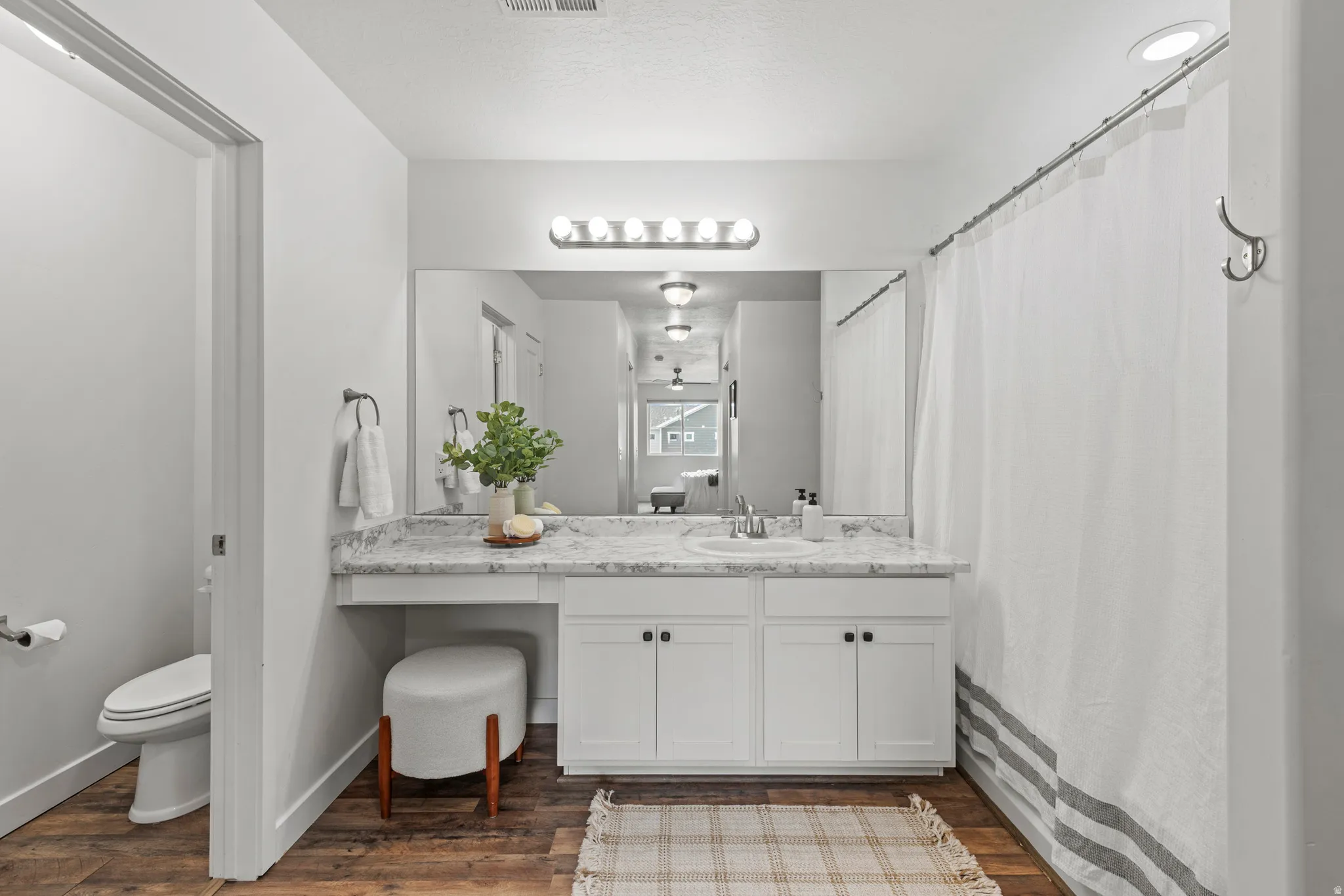 Bathroom featuring a white vanity with built-in storage, a light-toned countertop, a large mirror, a chrome-finish light fixture, and wood-finish flooring