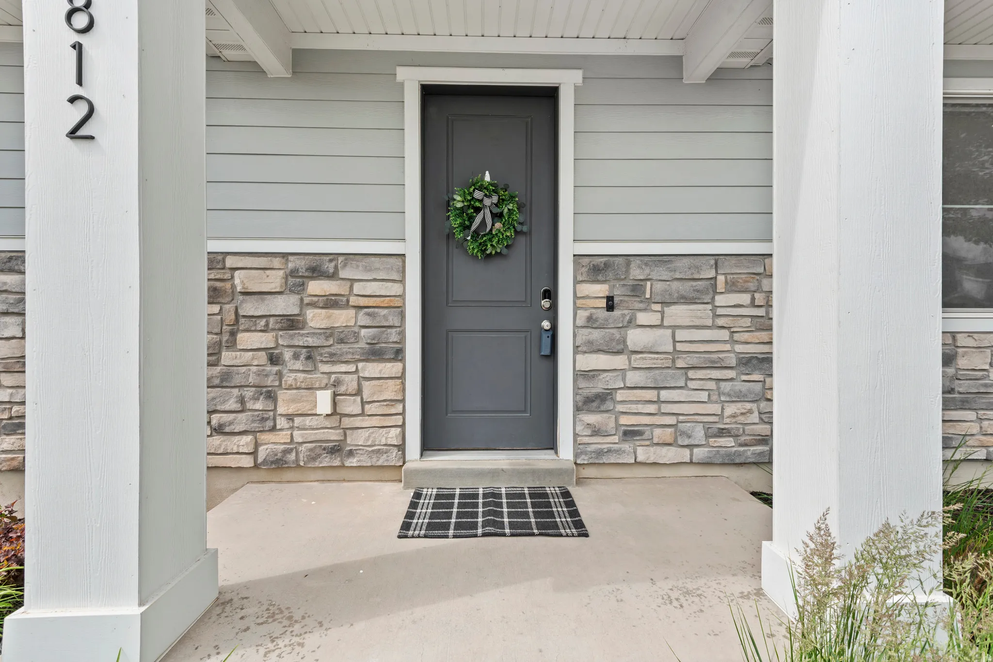 Exterior entry featuring a dark gray paneled door with smart lock hardware, light gray horizontal siding, and natural stone veneer accents