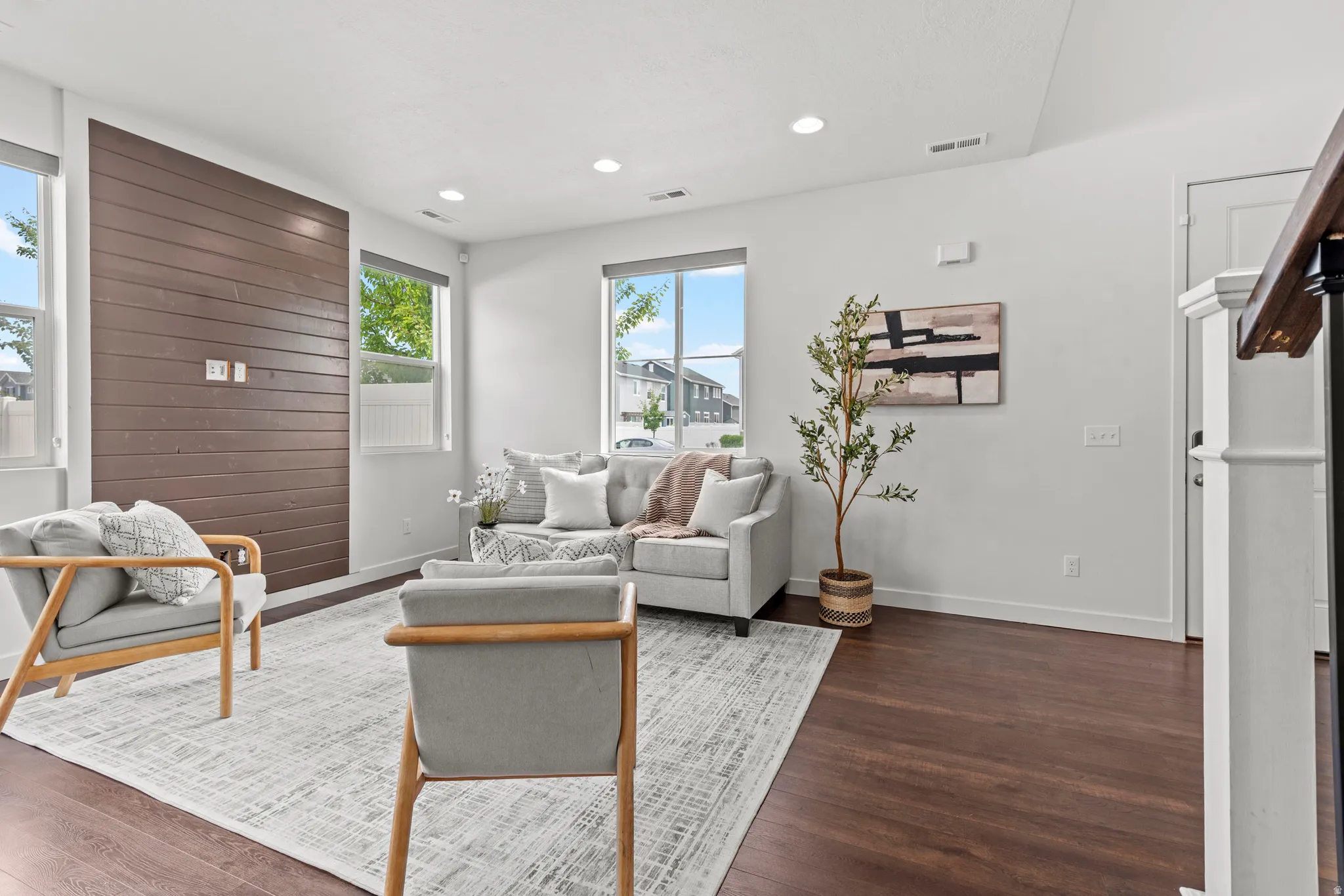 Living area featuring dark wood-finish flooring, a prominent accent wall with horizontal wood paneling, and multiple large windows