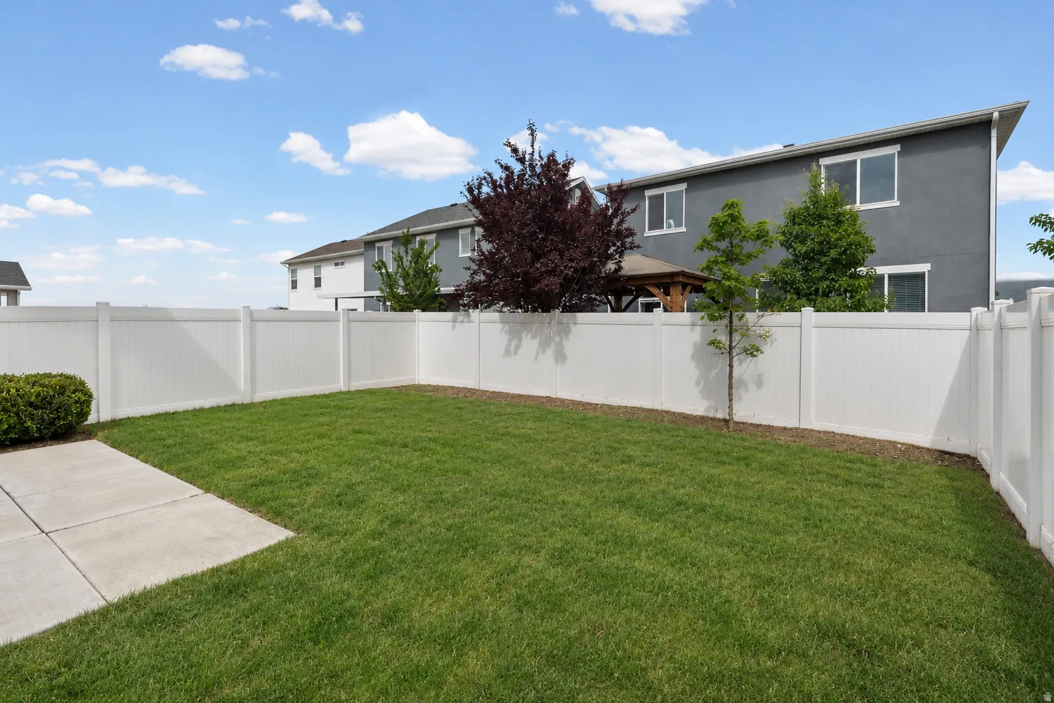 Expansive grassy yard enclosed by a white privacy fence, featuring a concrete patio section and established landscaping