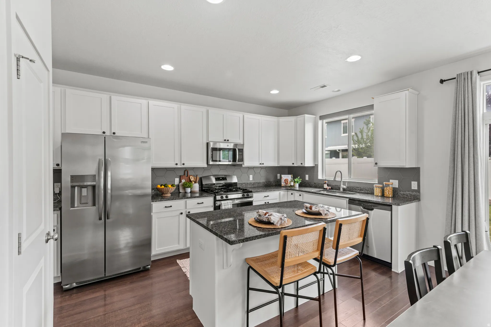 Modern kitchen featuring white shaker cabinetry, stainless steel appliances, dark granite countertops, a coordinating backsplash, and wood-finish flooring