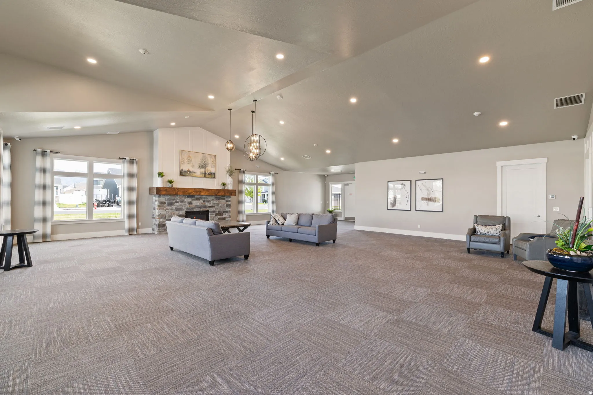 Spacious common area featuring a vaulted ceiling with recessed lighting, a stone-front fireplace with a wood mantle, and large windows