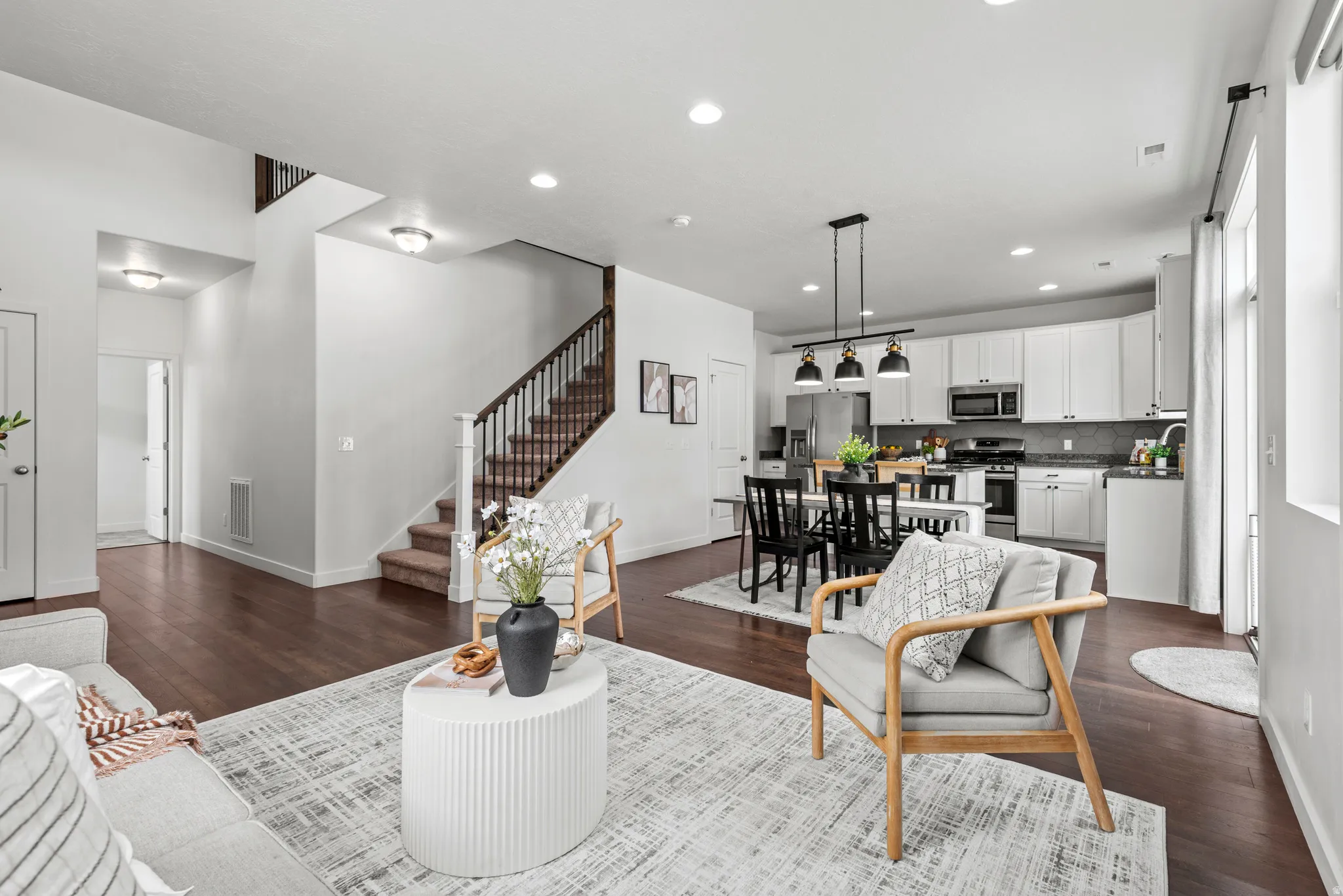 Open-concept living area featuring rich wood-finish flooring, a contemporary staircase with dark wood railings, and recessed ceiling lighting