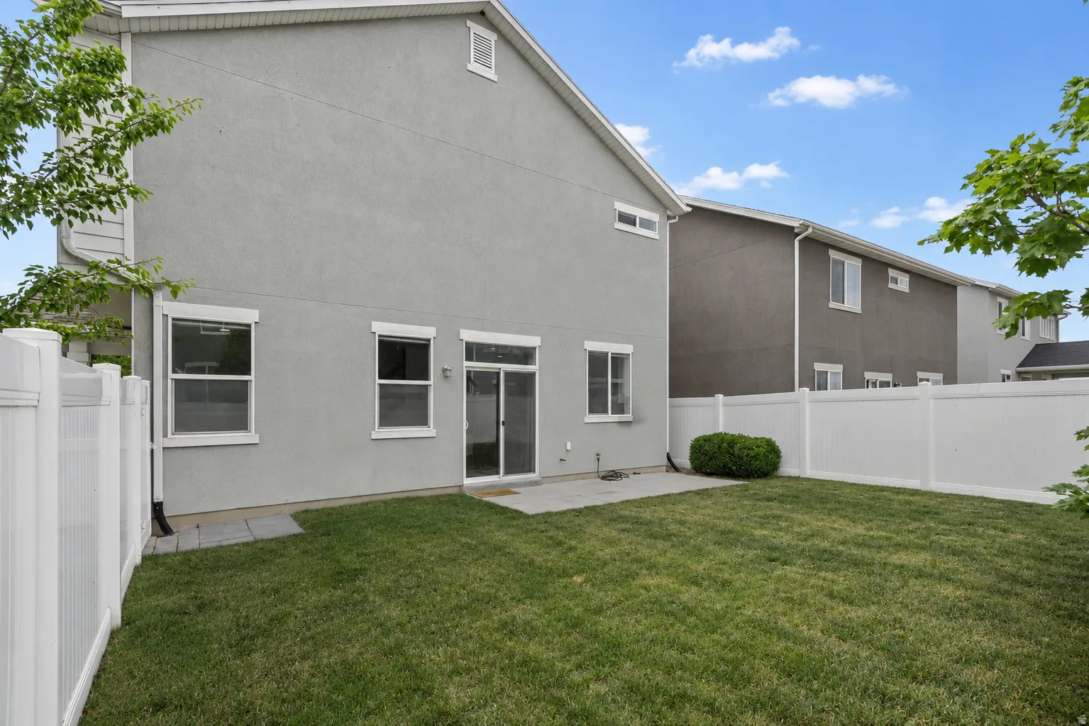 Private backyard with a manicured lawn, white vinyl fencing, and a concrete patio