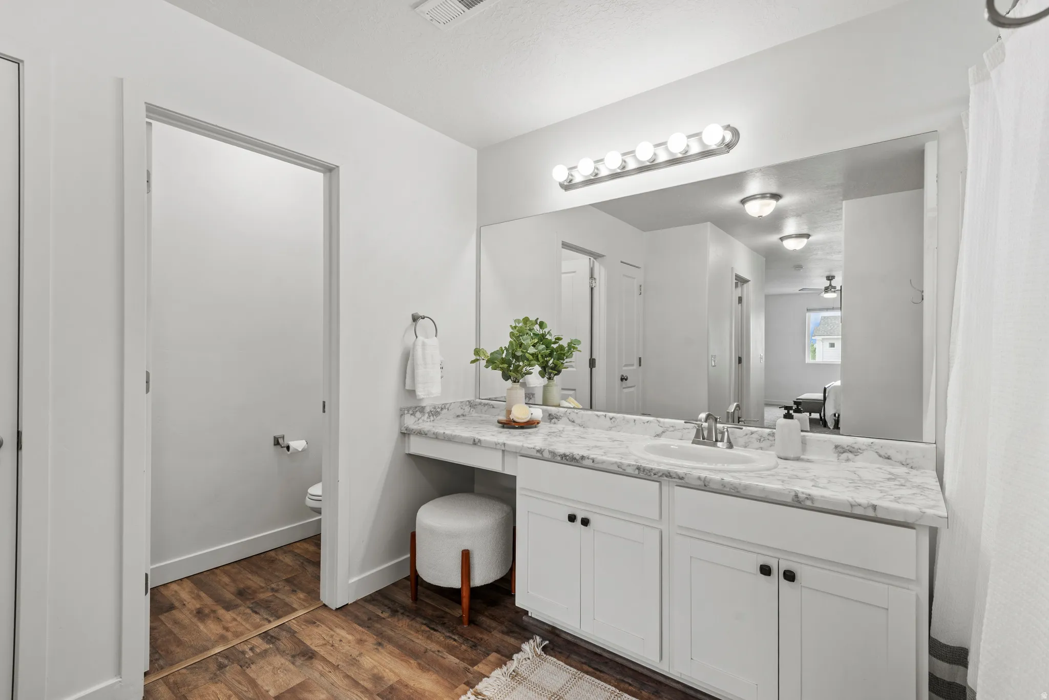 Bathroom featuring a single vanity with white cabinetry, a light-toned countertop, and wood-finish flooring