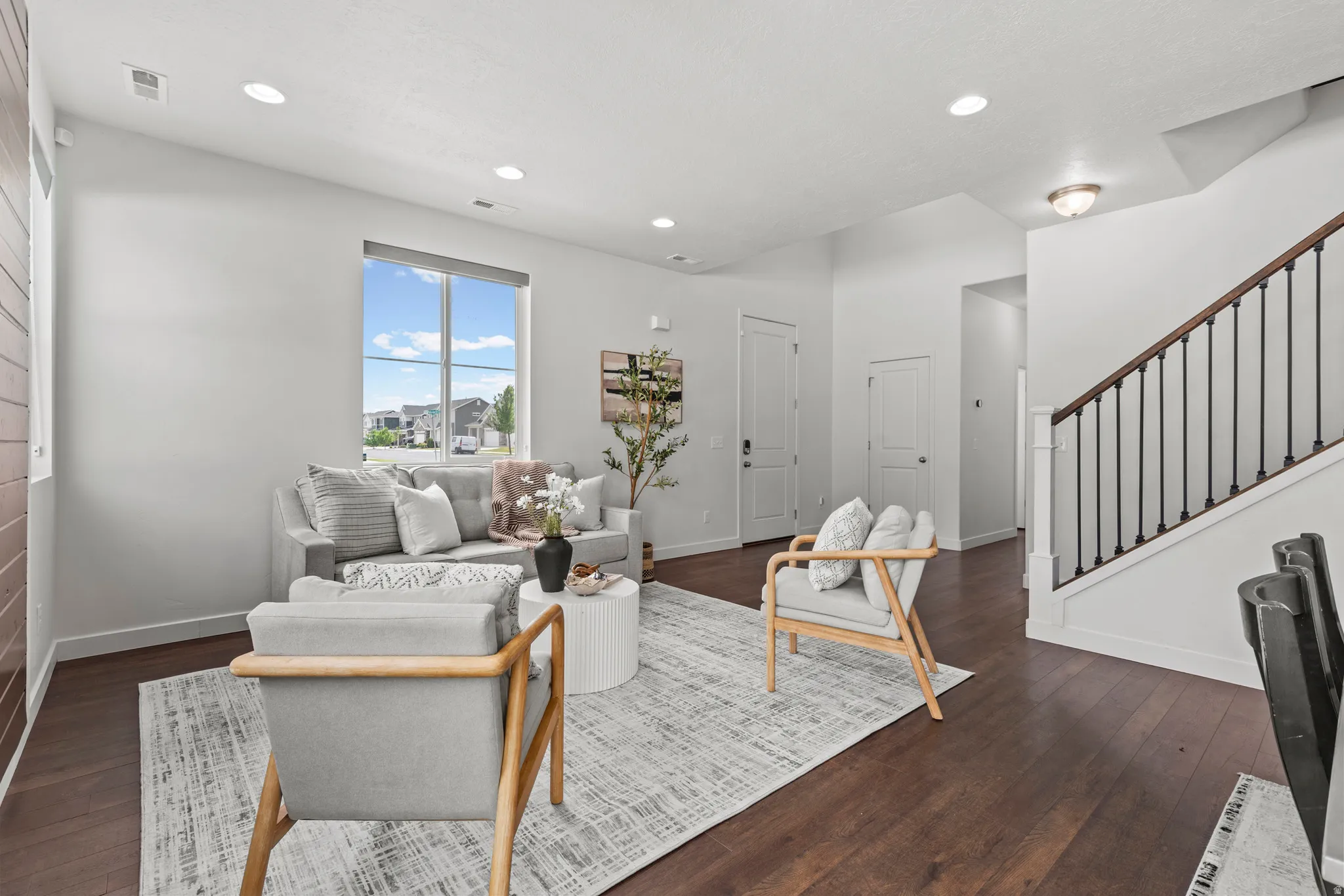 Living area featuring dark wood-finish flooring, a large window, recessed lighting, and a staircase with a dark wood handrail and black balusters