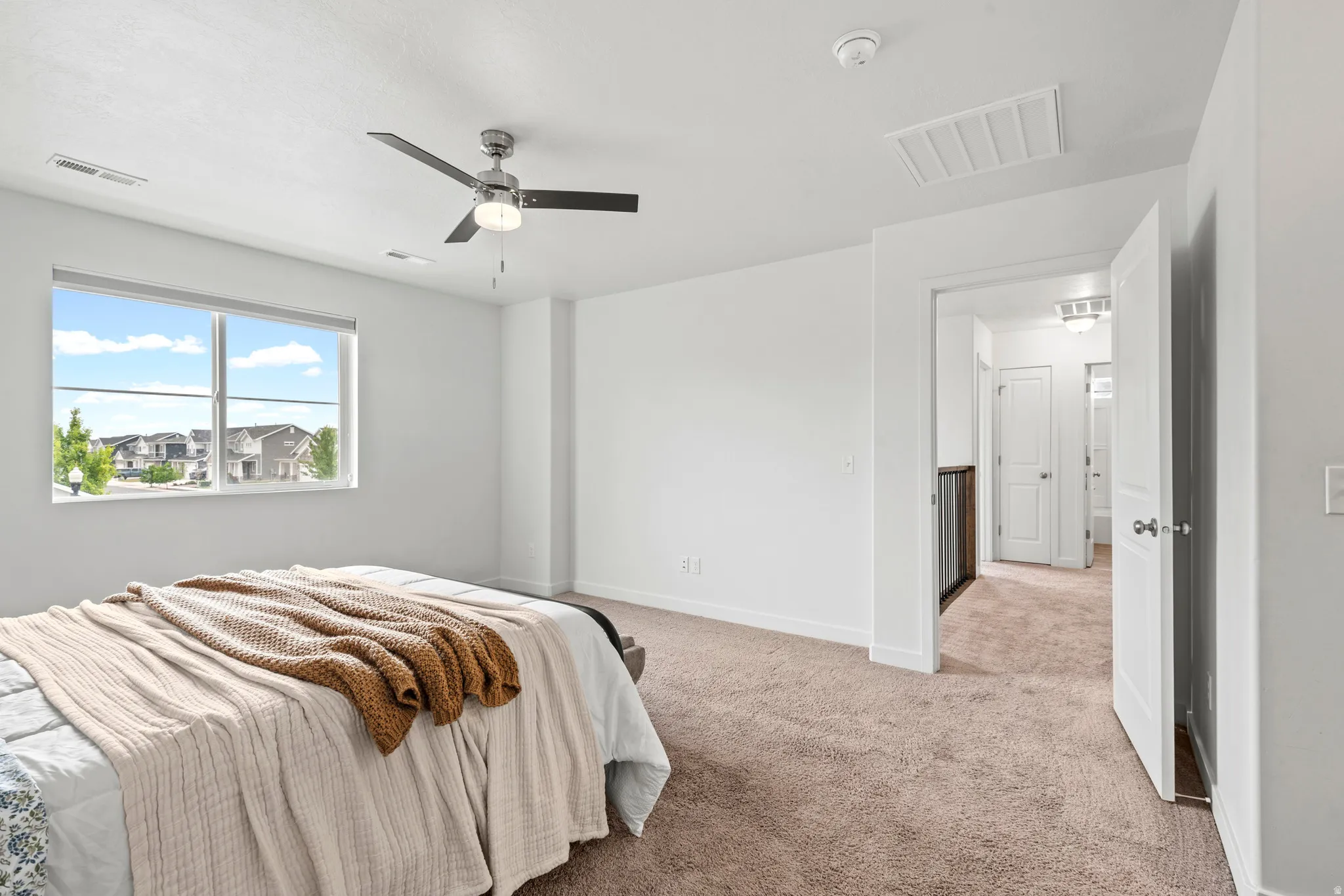 Spacious room featuring a large window, neutral carpeting, a modern ceiling fan, and white baseboards