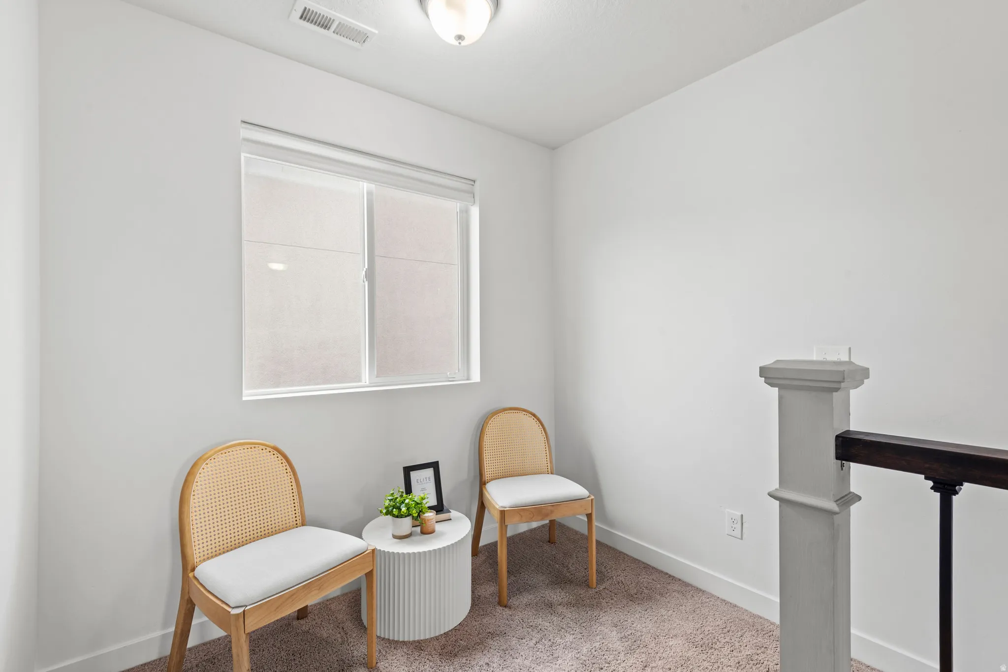 Bright interior space featuring a window with roller shades, neutral carpeting, white baseboards, and a contemporary ceiling light fixture