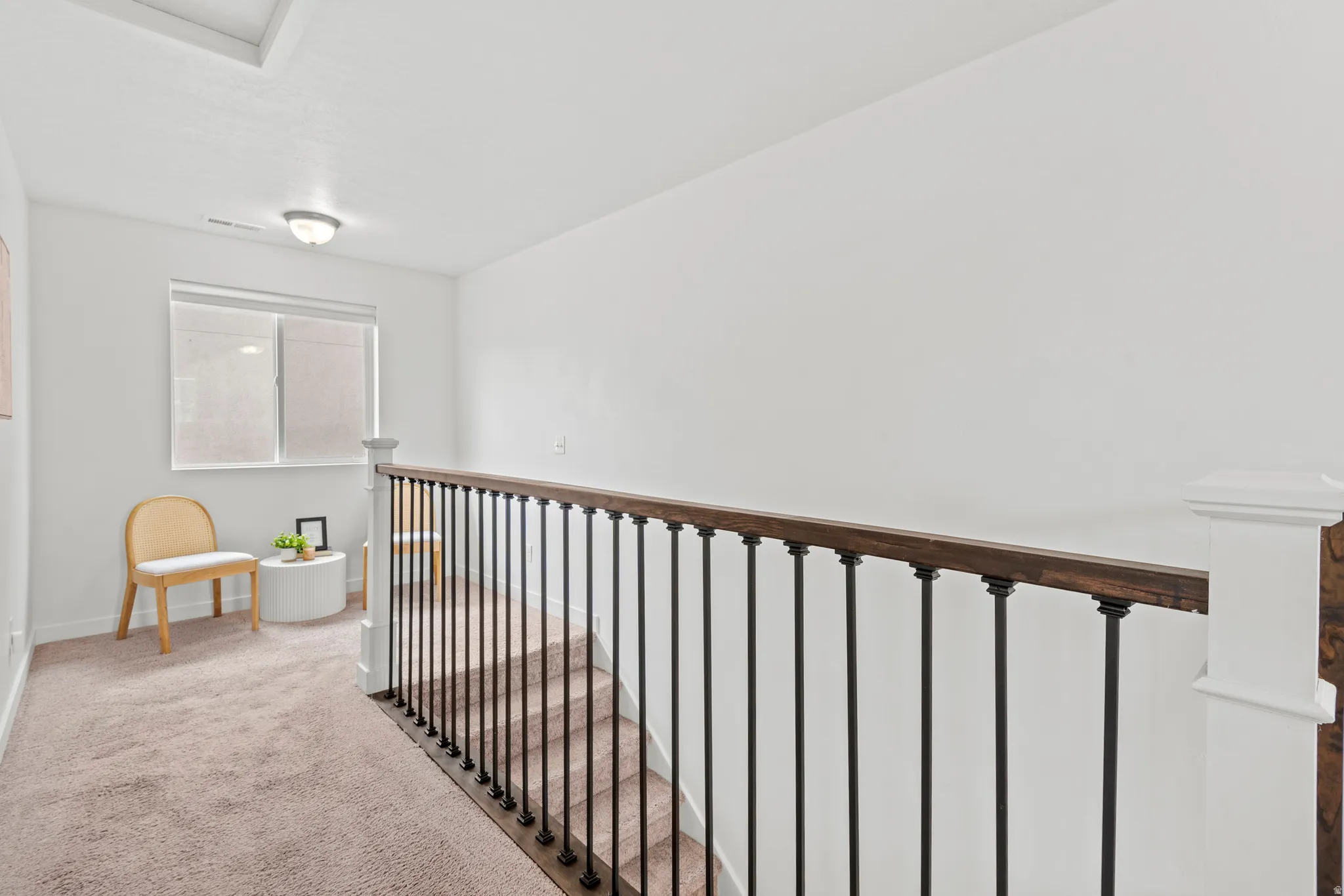 Carpeted hallway featuring a window with blinds, a flush mount light fixture, and a staircase with dark wood railing and black balusters