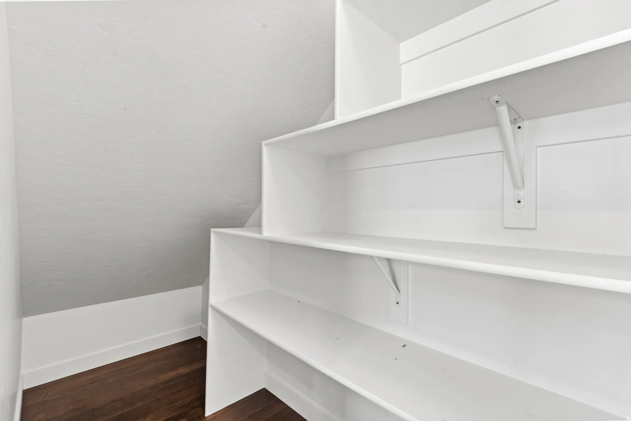 Built-in shelving with multiple white shelves, white wall paneling, and dark wood-finish flooring