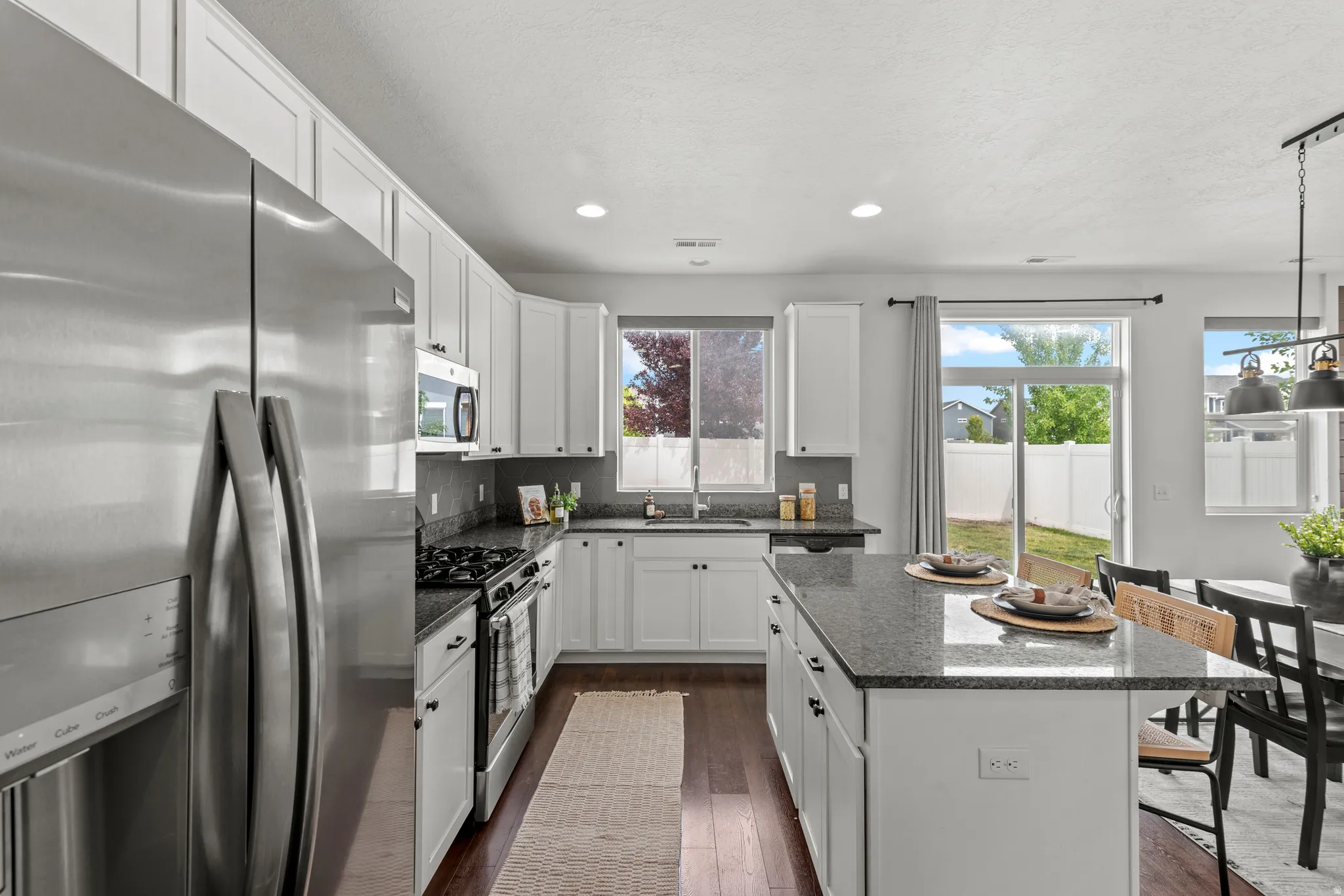 Modern kitchen featuring white cabinetry, stainless steel appliances, dark stone countertops, wood-finish flooring, and recessed lighting